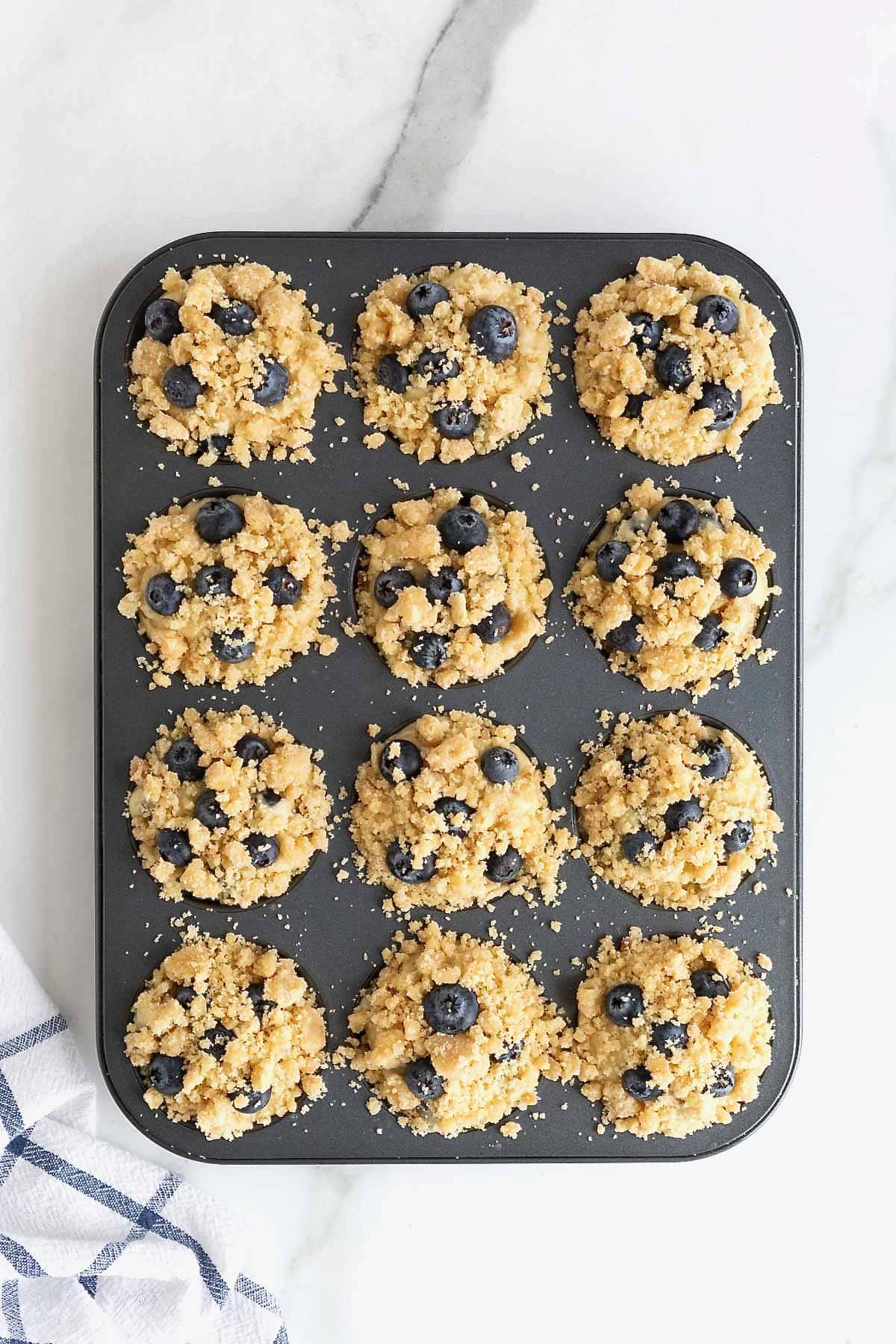 Blueberry streusel muffins ready to bake in an aluminum muffin tin.