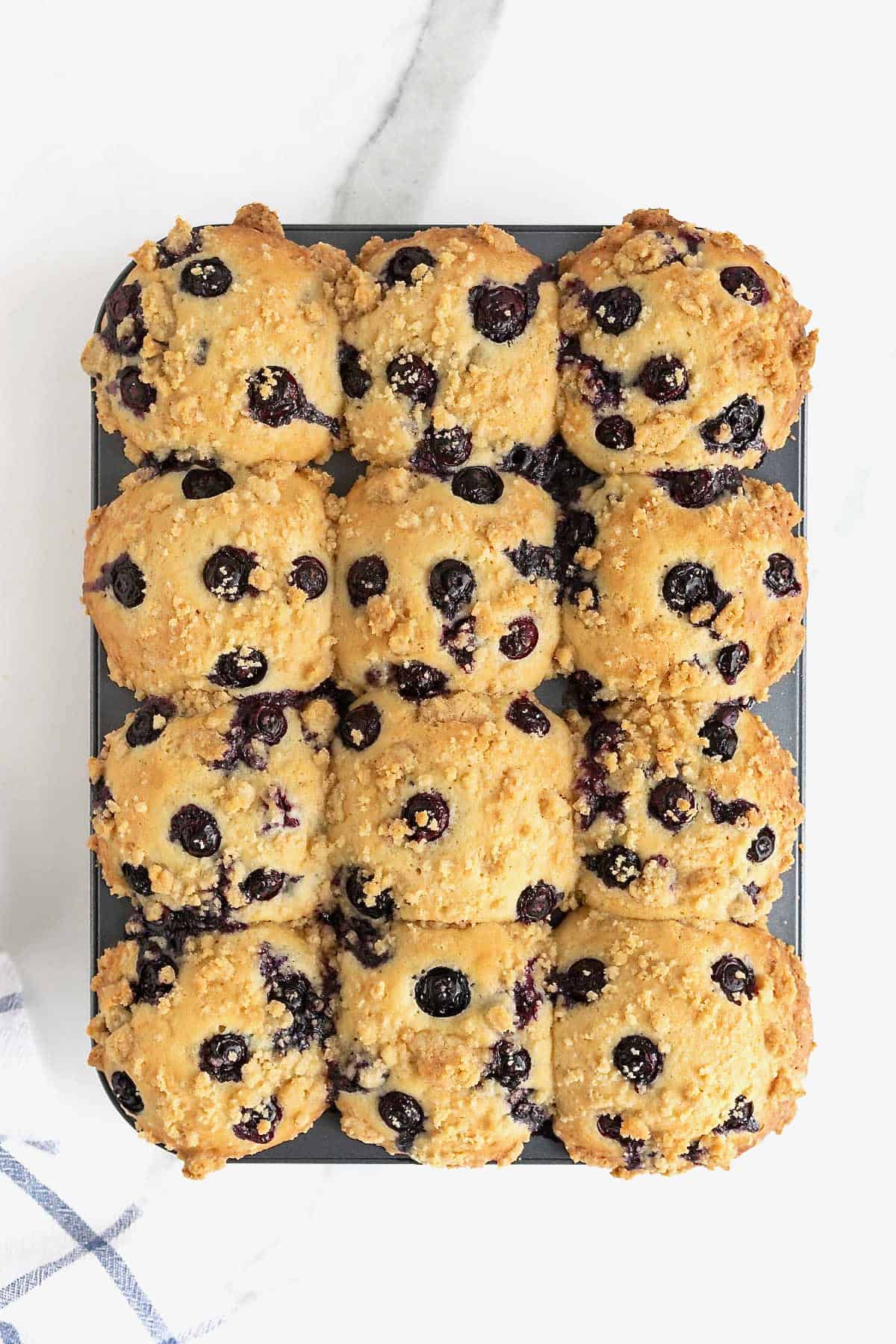 A aluminum muffin tin full of fresh baked blueberry streusel muffins.