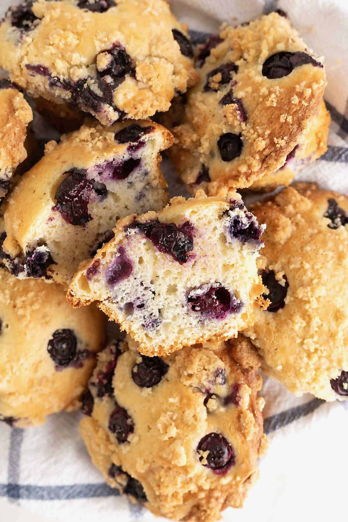 A blueberry muffin cut in half on top of a pile of blueberry muffins.
