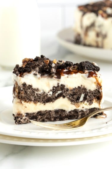 A slice of pie with an Oreo crust, ice ream filling, and crushed Oreos on top on a white plate with a fork.