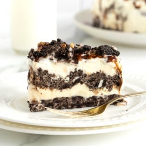 A slice of Oreo Ice Cream pie with an Oreo crust, ice ream filling, and crushed Oreos on top on a white plate with a fork.