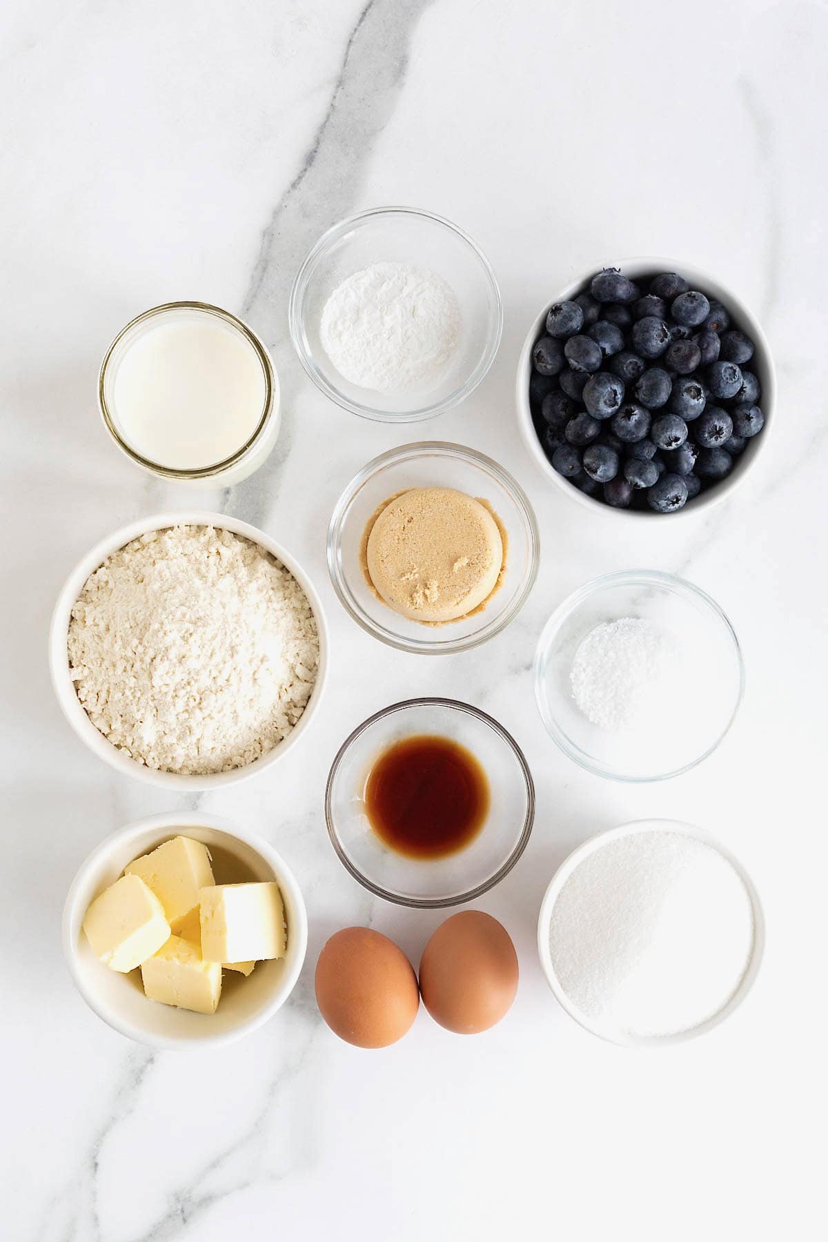 Ingredients to make blueberry streusel muffins in small glass dishes on a white marble counter.