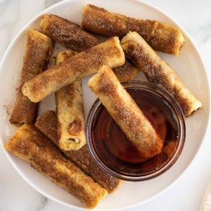 Cinnamon sugar covered French toast roll ups surrounding a glass bowl of warmed maple syrup.