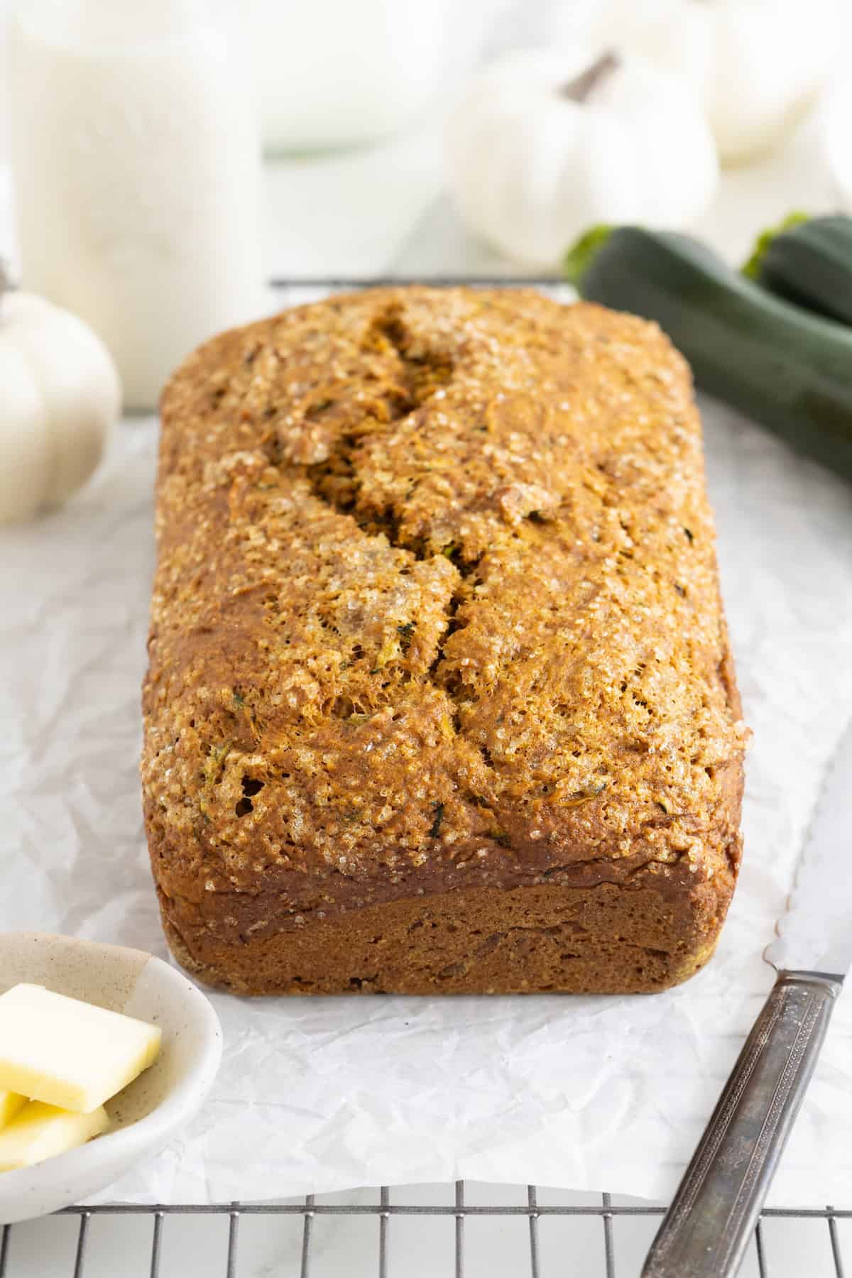 A loaf of pumpkin zucchini bread on a parchment lined wire cooling rack.