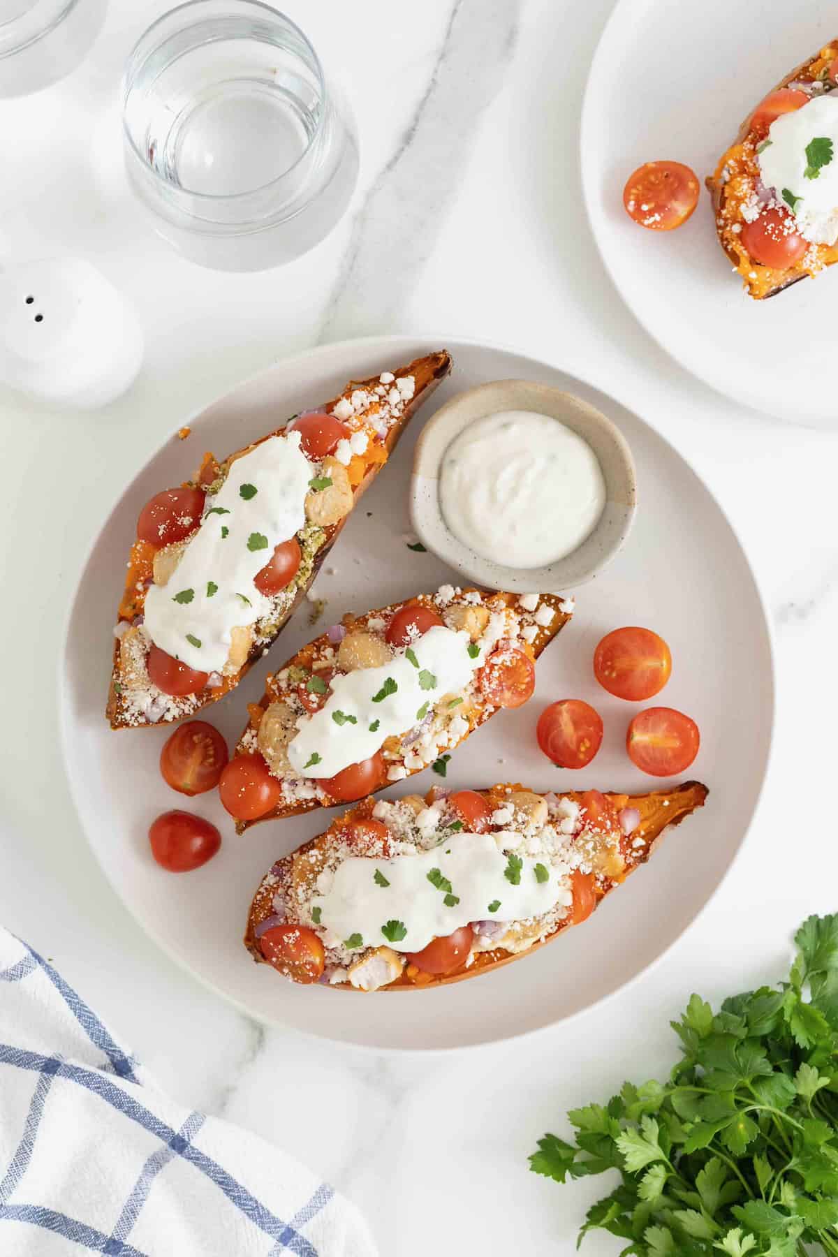 Three Greek loaded sweet potatoes on a large white plate next to a small dish of tzatziki sauce.