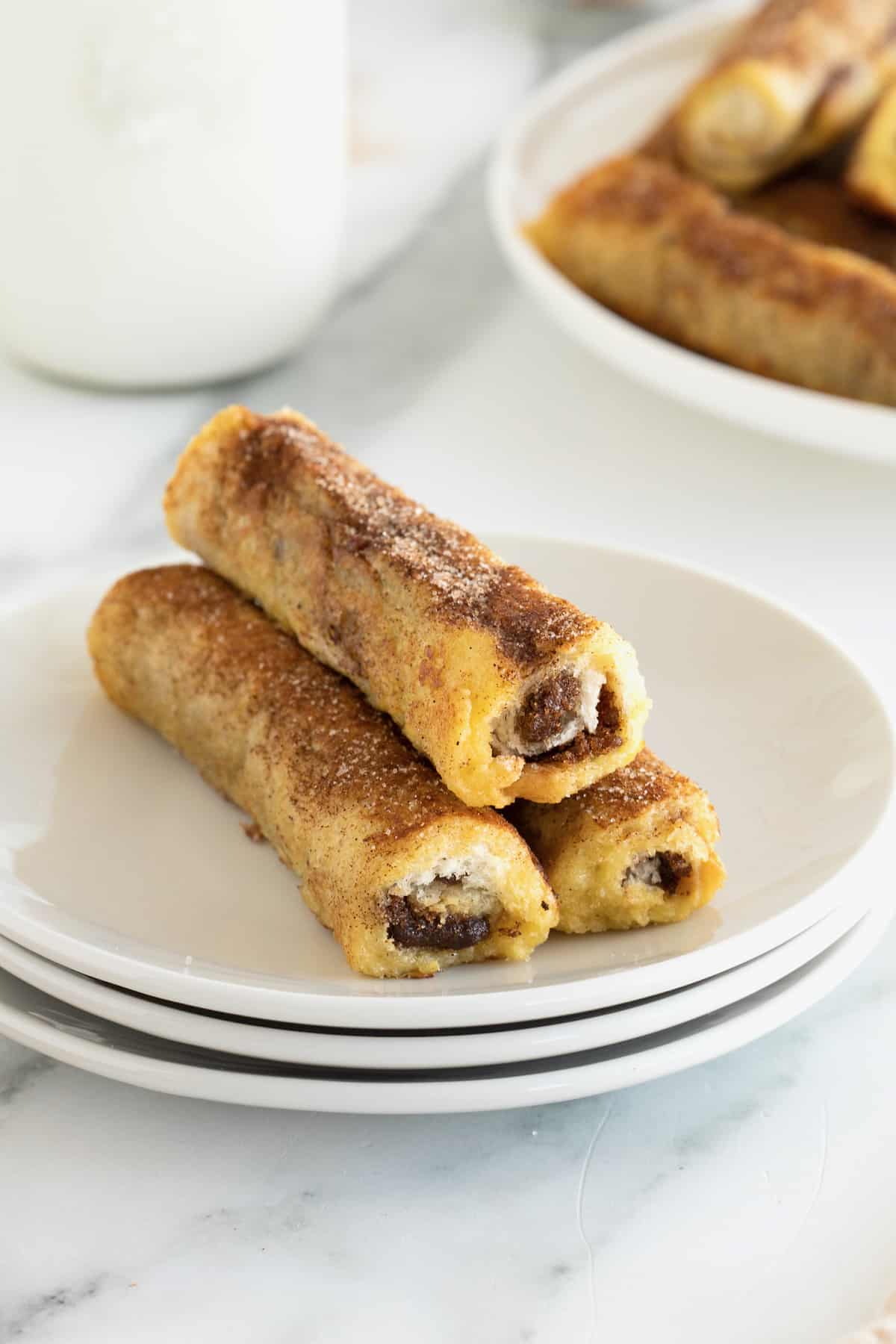 A pile of 3 French toast roll ups on a stack of 3 white plates.