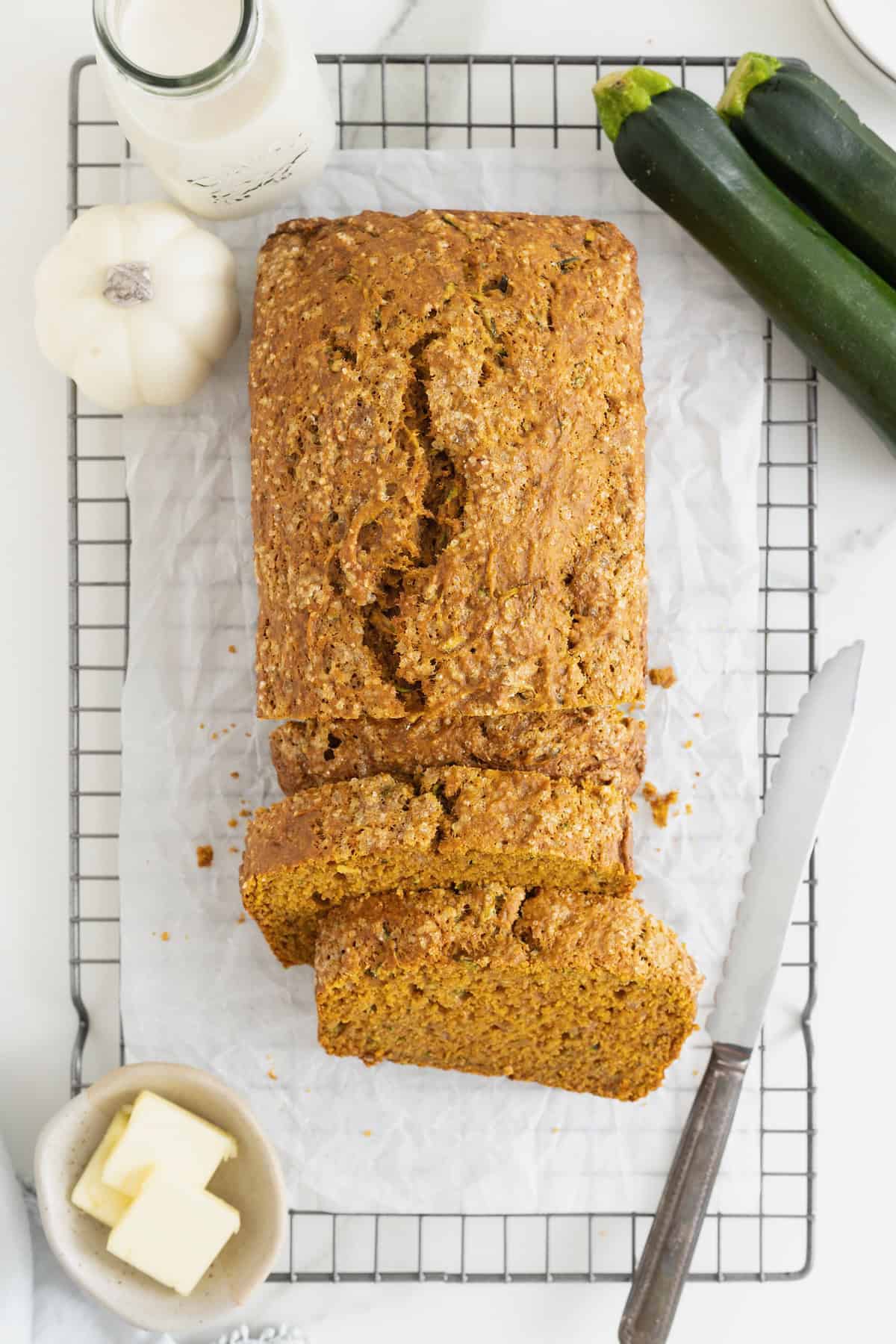 A loaf of pumpkin zucchini bread on a wire cooling rack.