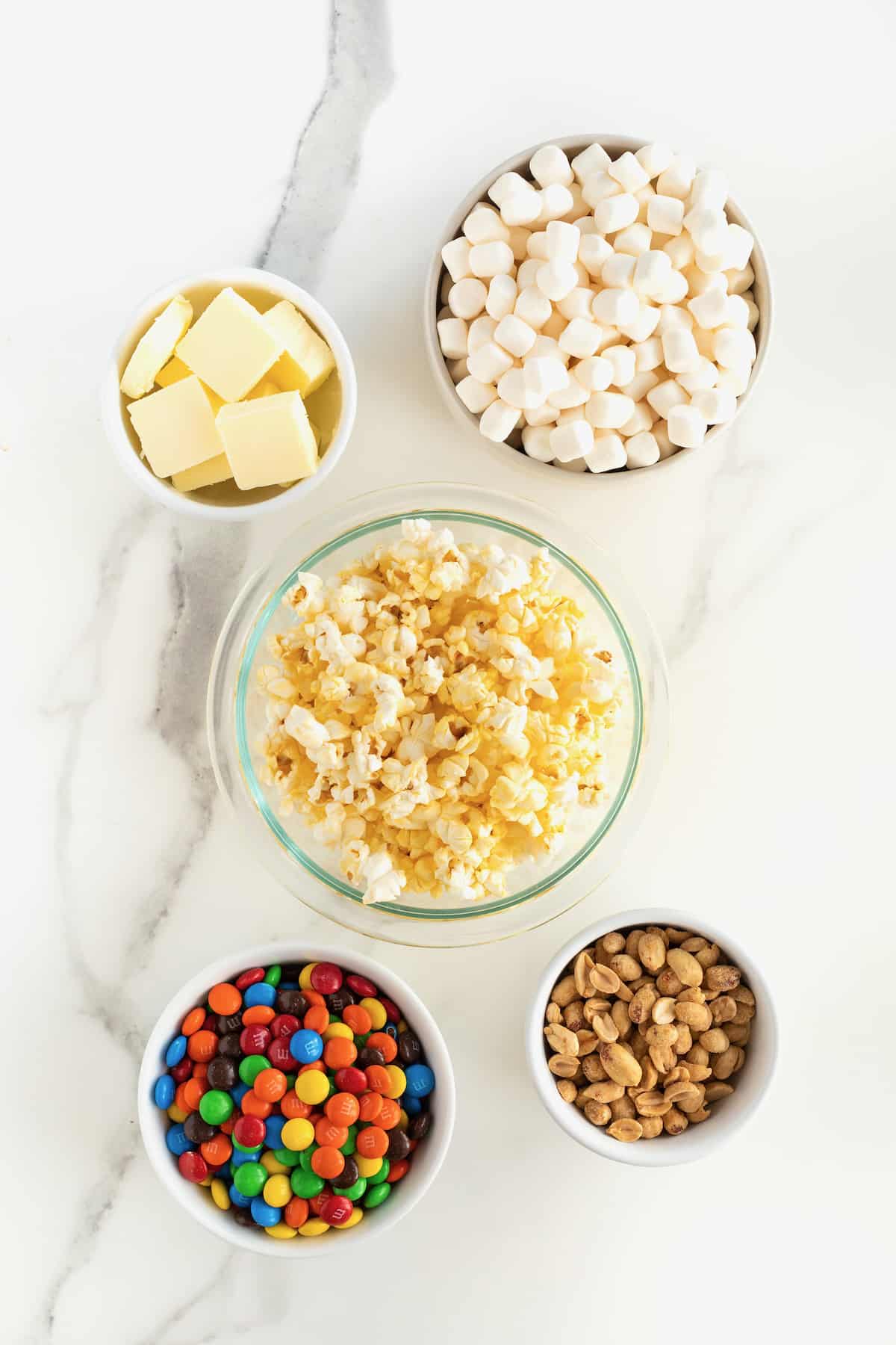 Ingredients for peanut popcorn cake in small glass dishes on a white marble counter.