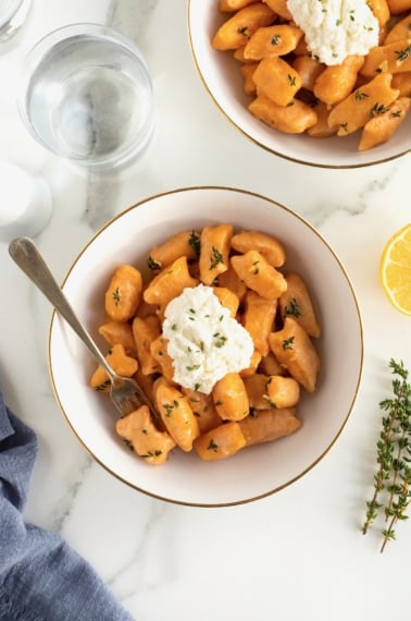 A gold-rimmed white bowl of sweet potato gnocchi with a dollop of fresh ricotta on top.