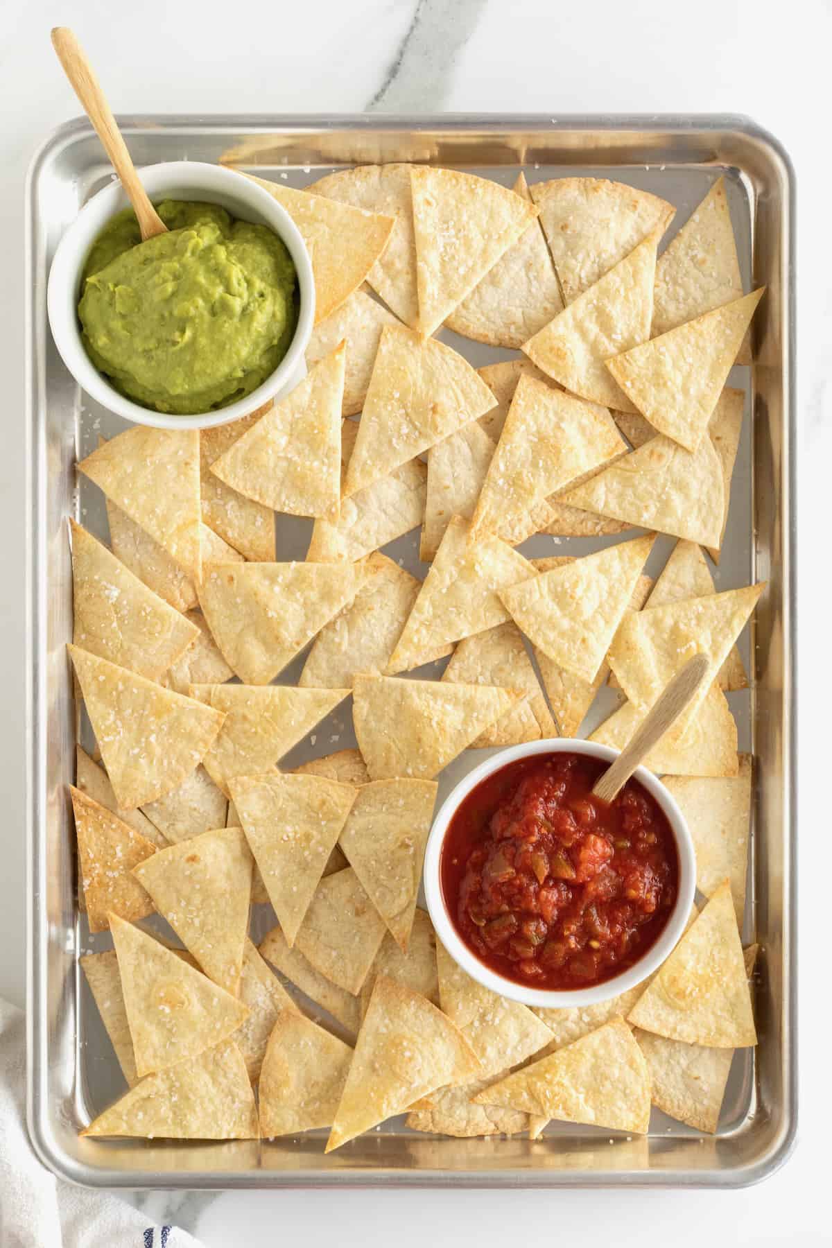 Baked triangle-cut flour on a baking sheet with a small bowl of salsa and a small bowl of guacamole.