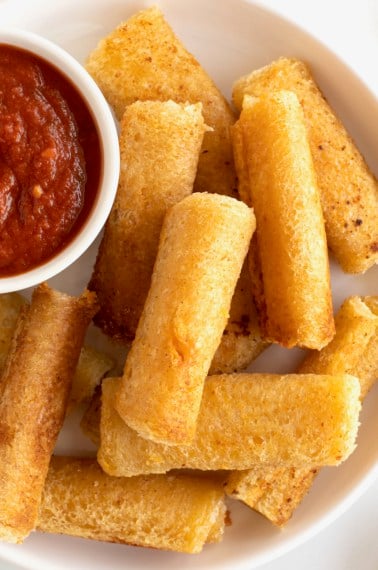 A large white serving plate with a pile of grilled cheese roll ups and a small dish of marinara sauce.