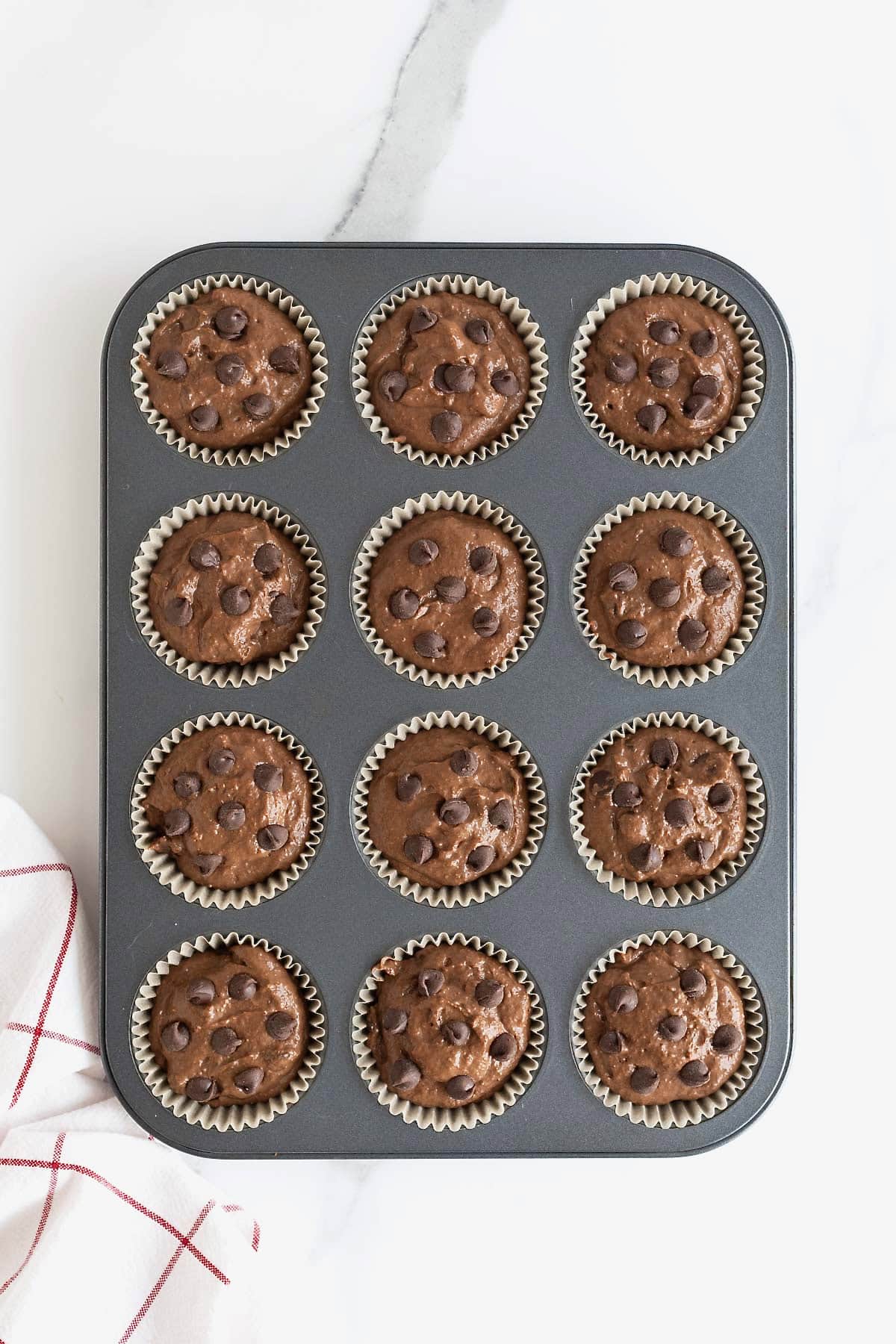A dark aluminum muffin tin of double chocolate muffin batter.