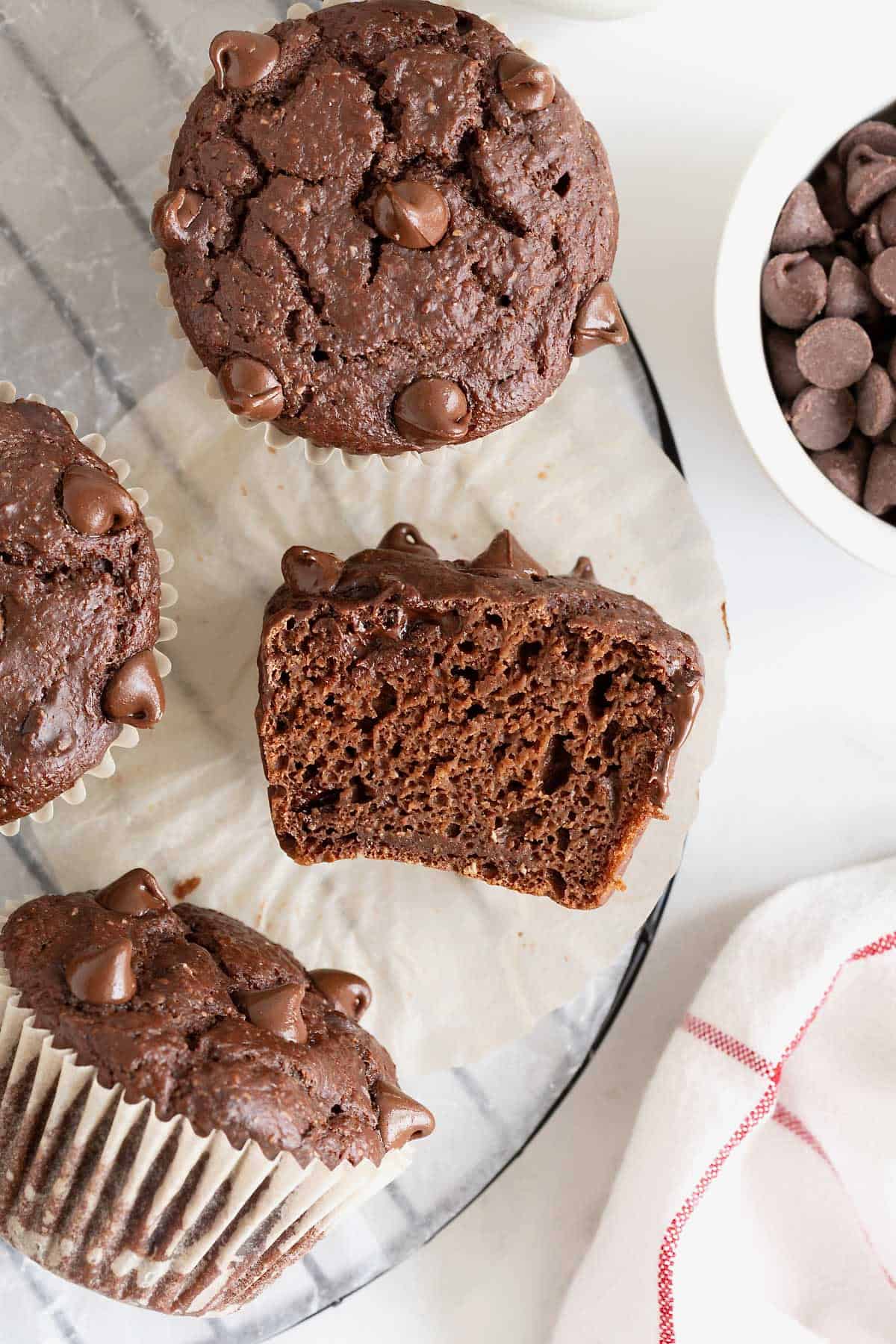 A round wire cooling rack scattered with chocolate muffins. One of the muffins is cut in half.