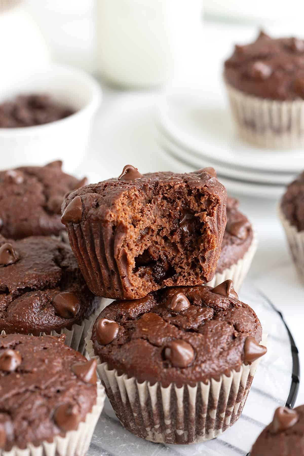 Chocolate muffins piled on a round wire cooling rack. The top muffin has a bite out of it.
