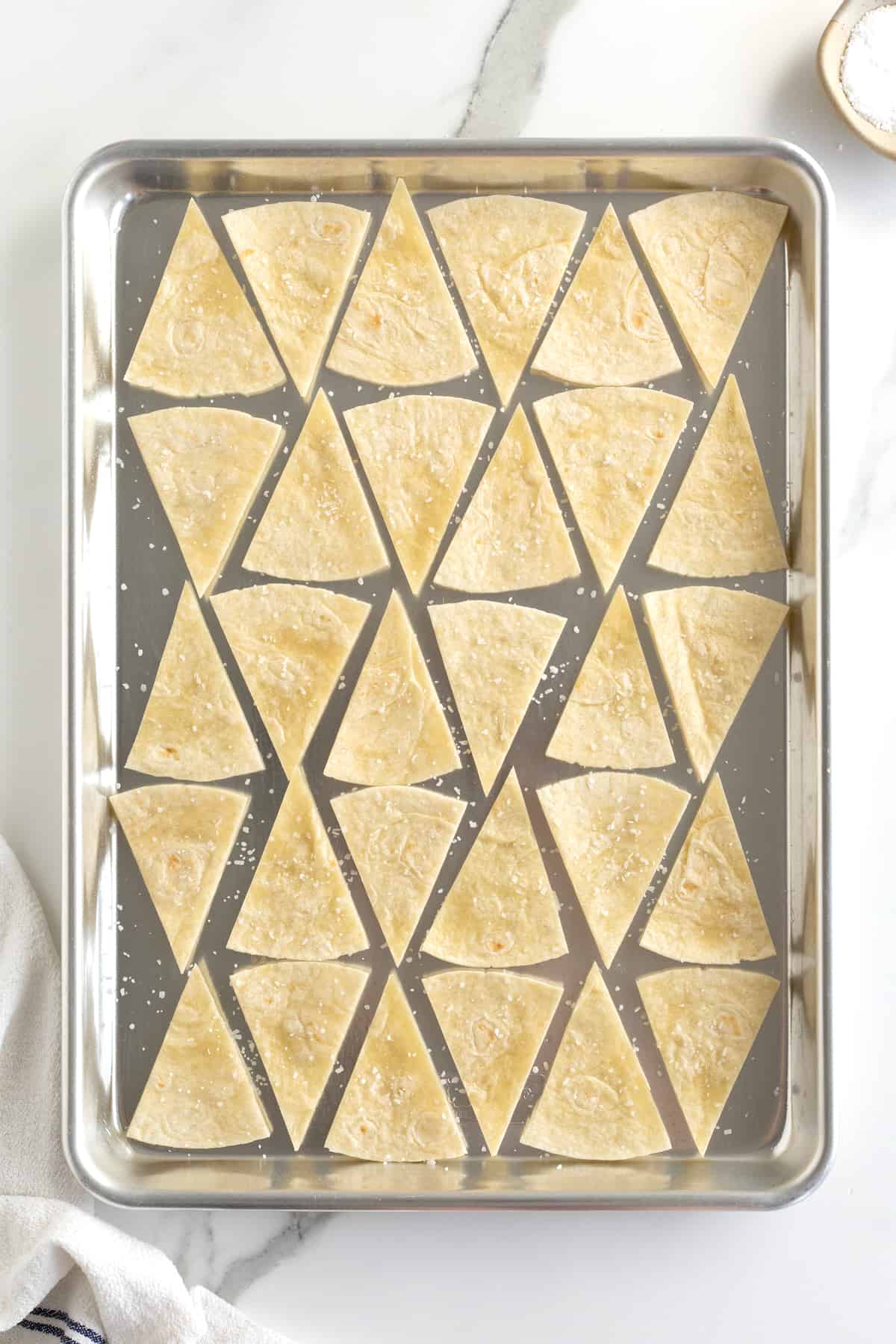 Triangle-cut tortillas on a baking sheet sprinkled with sea salt.