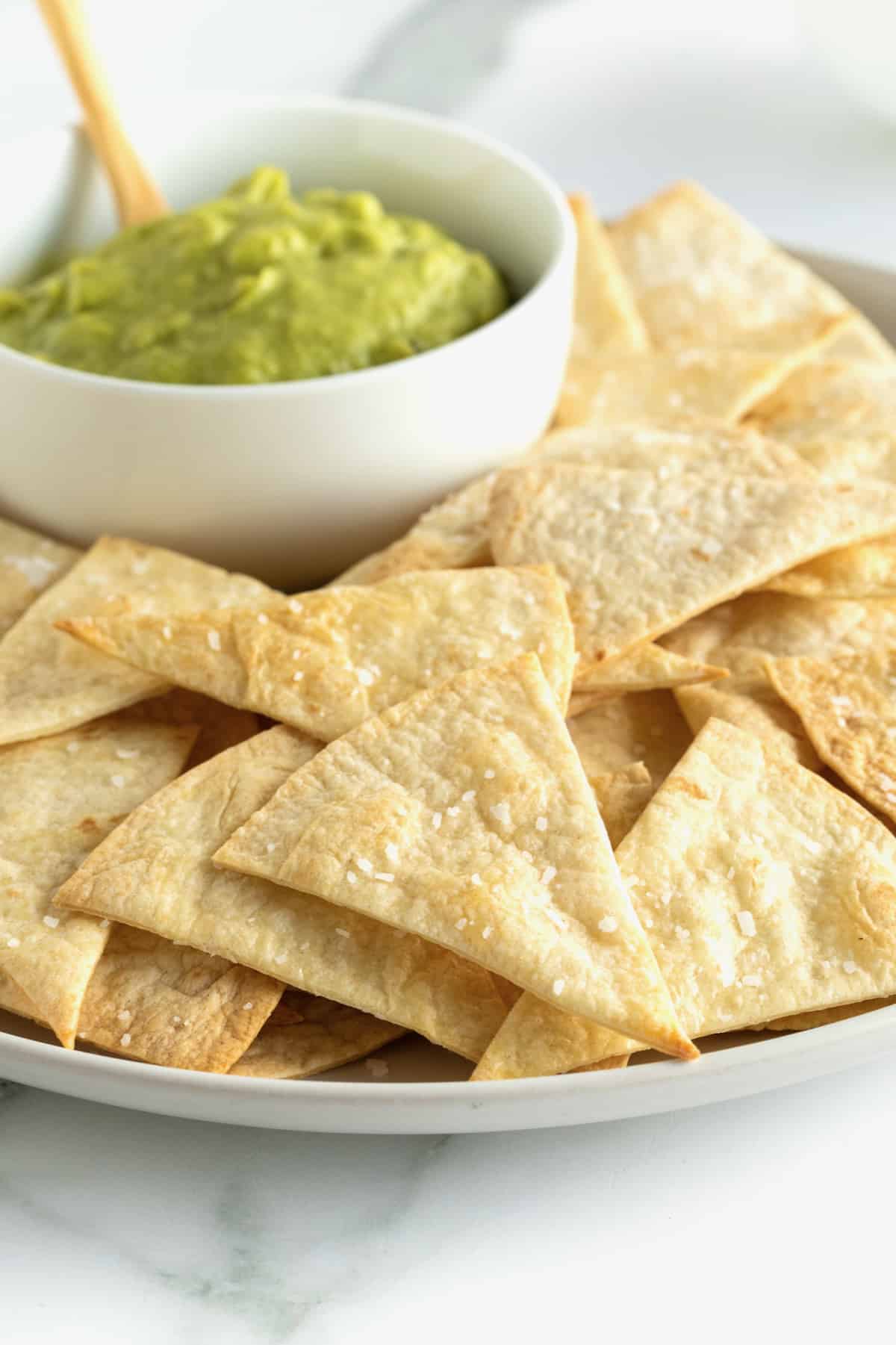 A plate of baked flour tortilla chips with a bowl of guacamole.