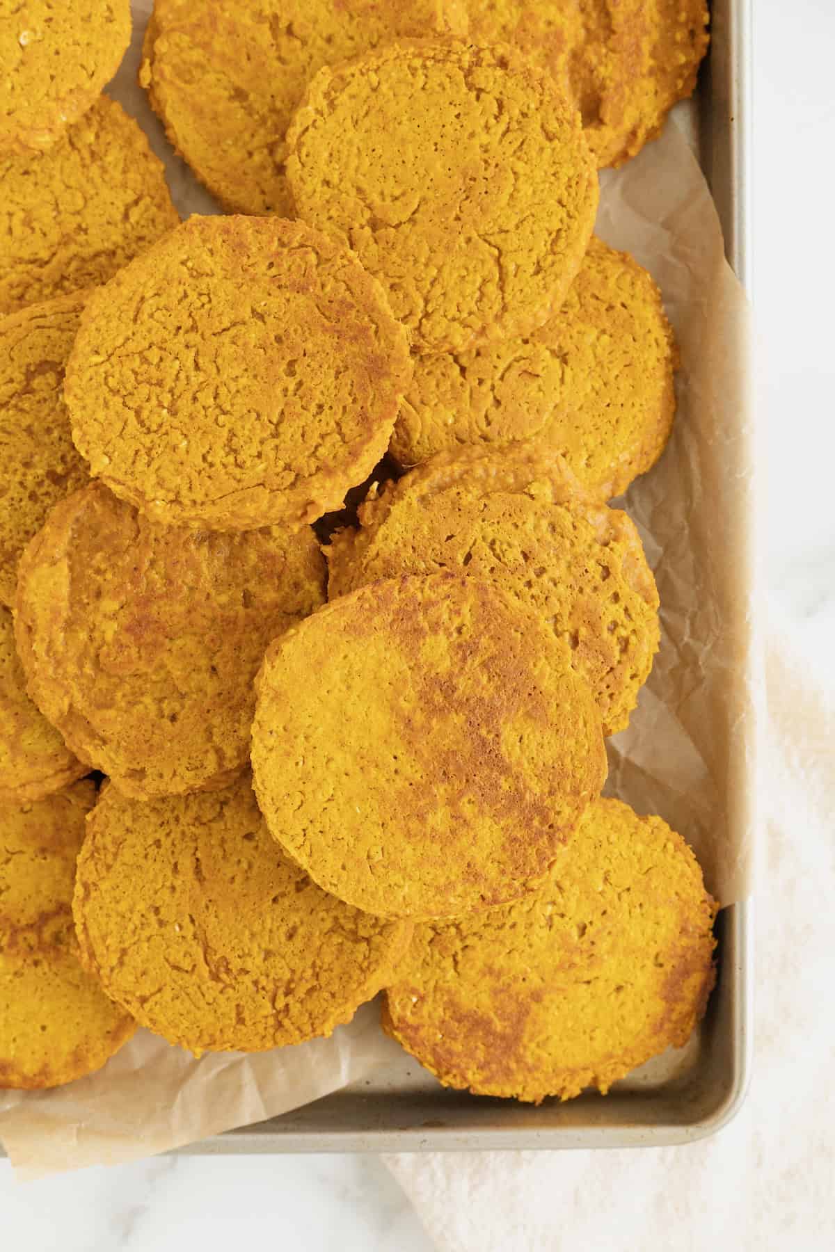 A pile of pumpkin oatmeal blender pancakes on an aluminum baking sheet.