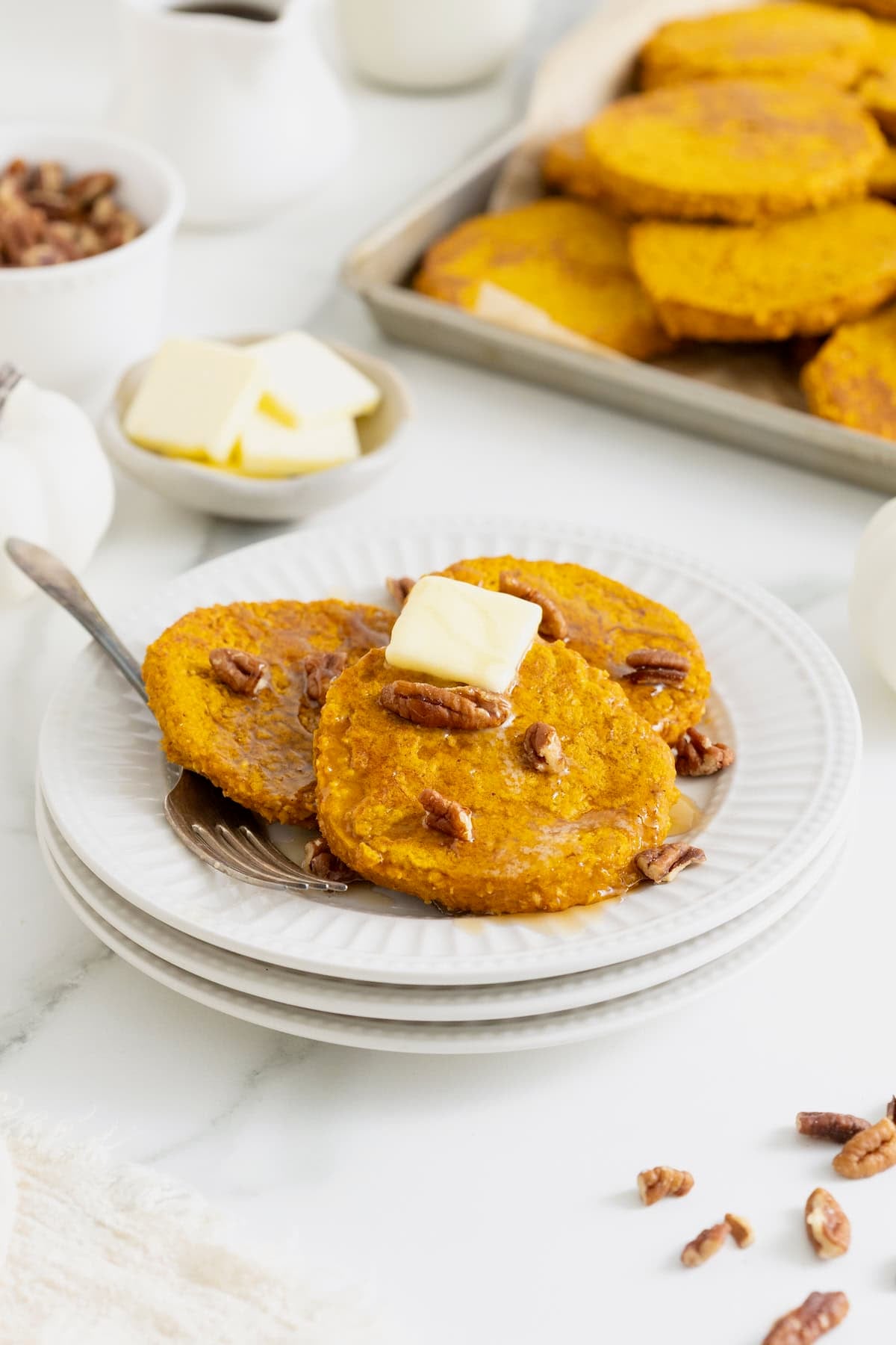 Three pumpkin oatmeal pancakes topped with a pat of butter on a white plate.