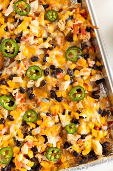 An aluminum sheet pan filled with nachos topped with cheese, black beans and jalapeño slices.