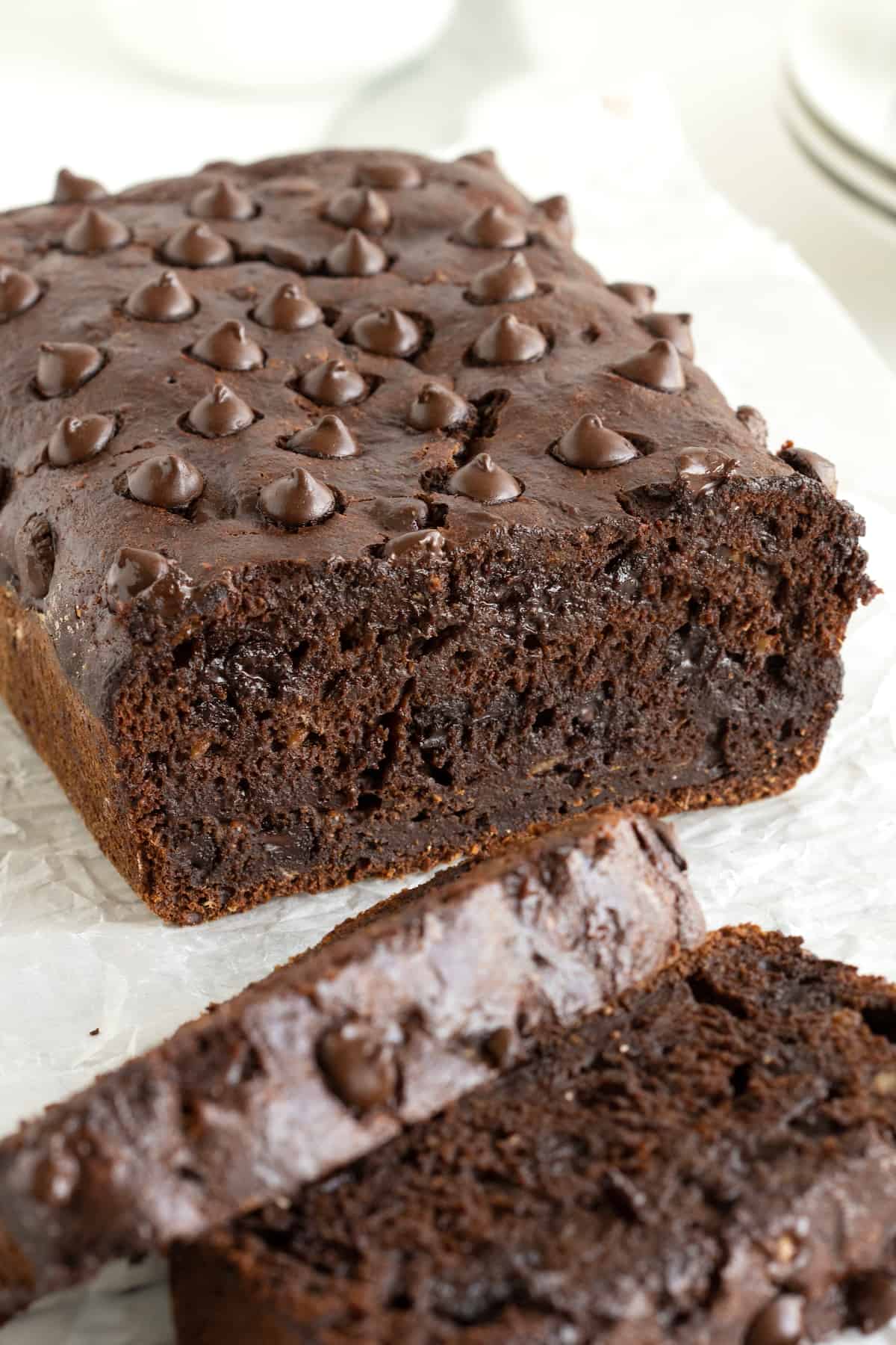 A loaf of chocolate banana bread sliced with a knife on a floured surface.