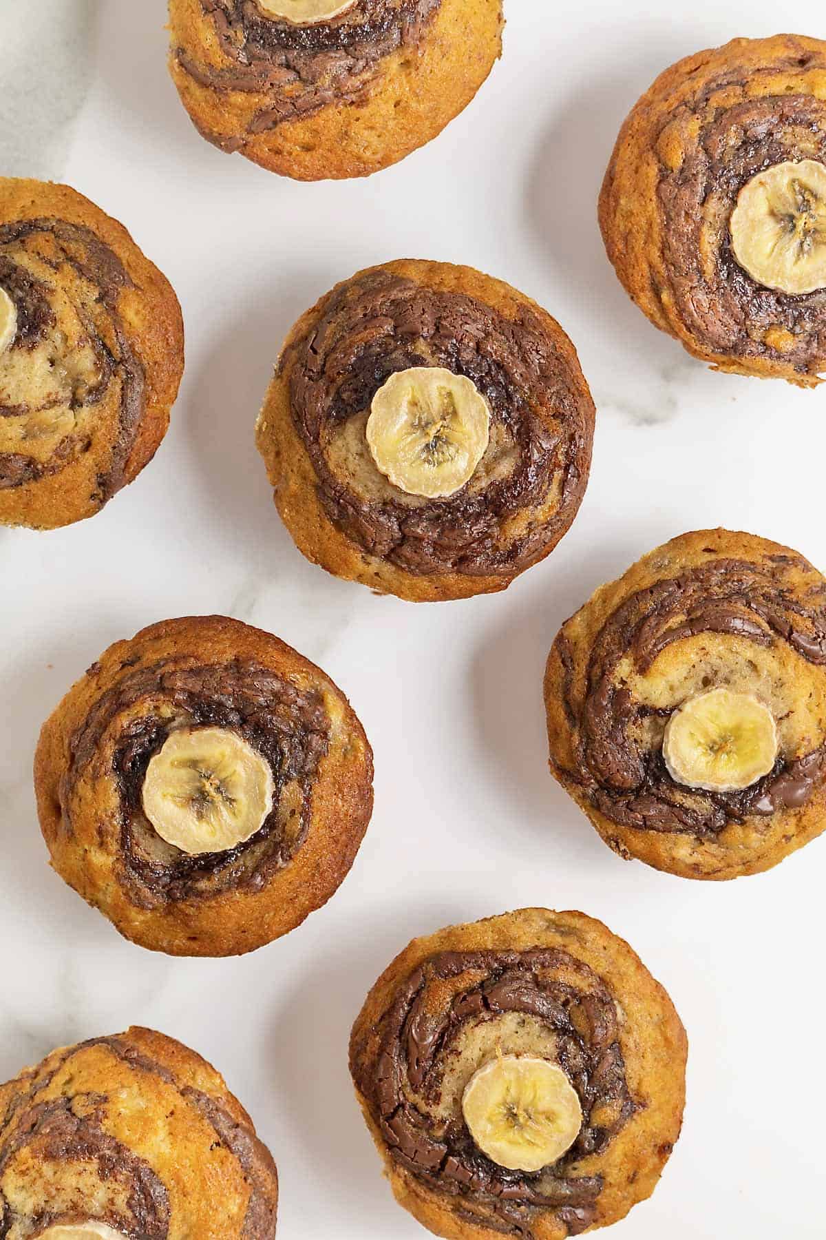 Eight Nutella swirled banana muffins on a white marble counter.