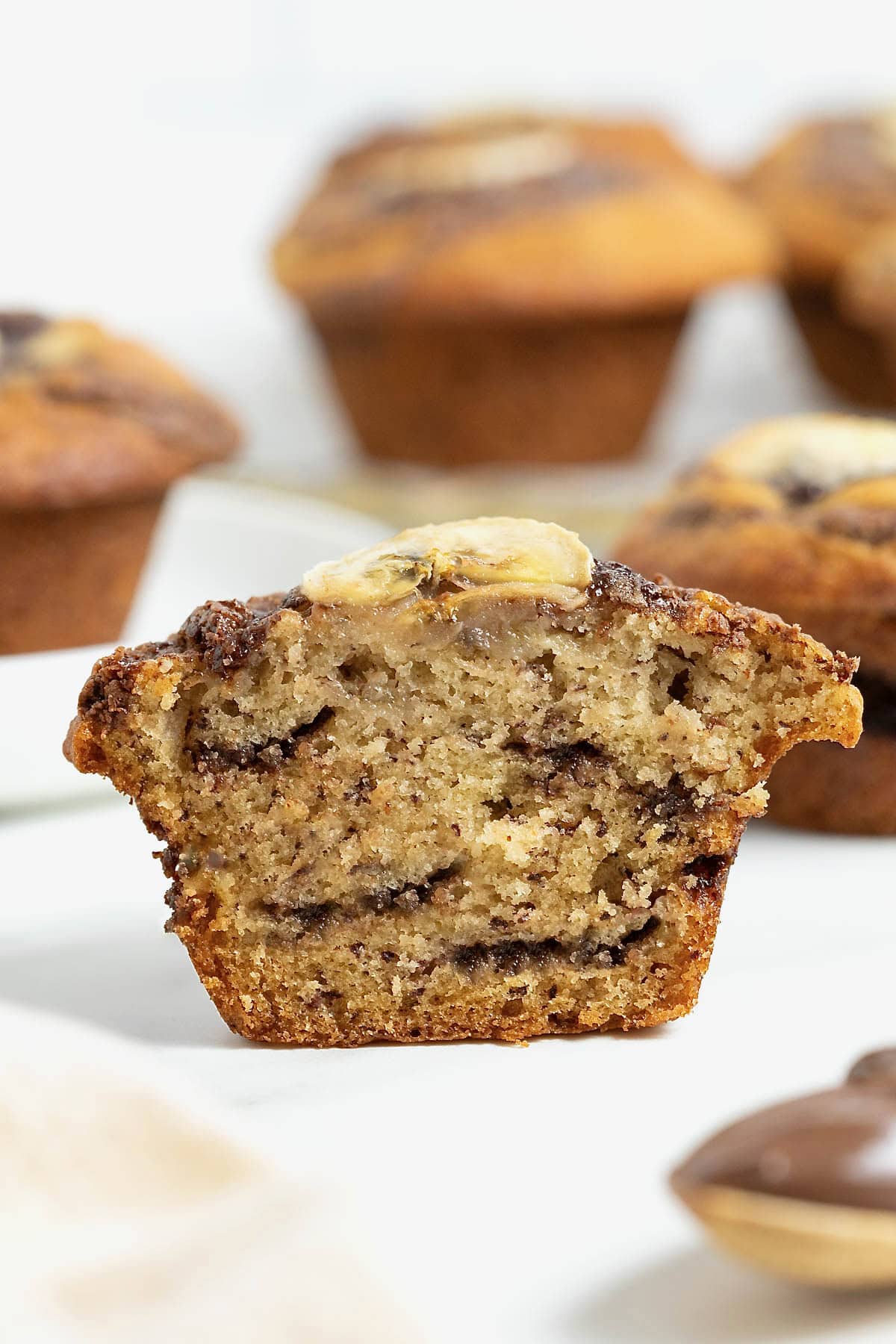 A nutella swirled banana muffin cut in half on a white marble counter.