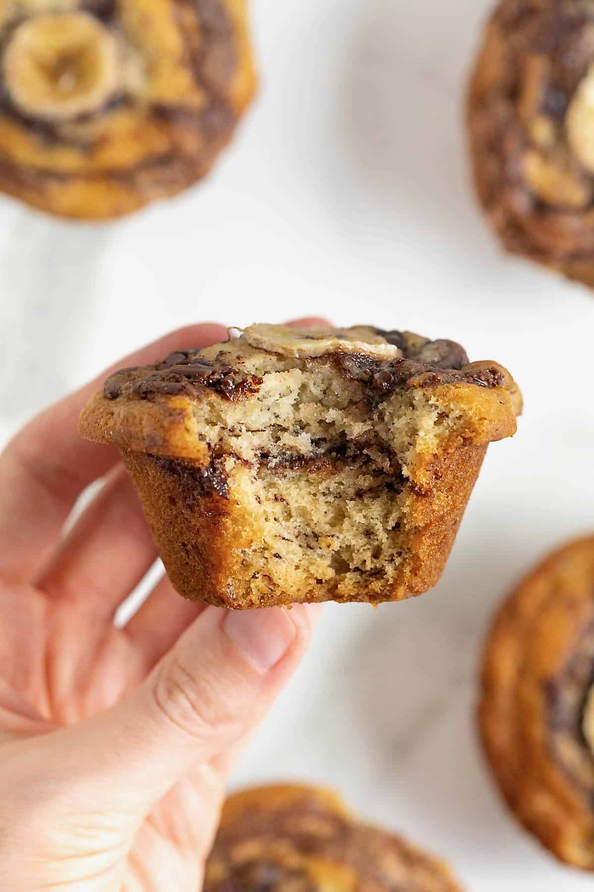 A hand holding a nutella swirled banana muffin with a bite out of it.