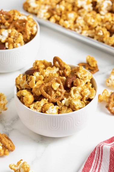 A bowl of caramel corn mixx in a small white bowl on a white marble counter.