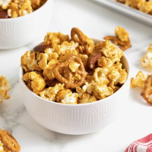 A bowl of caramel corn mixx in a small white bowl on a white marble counter.