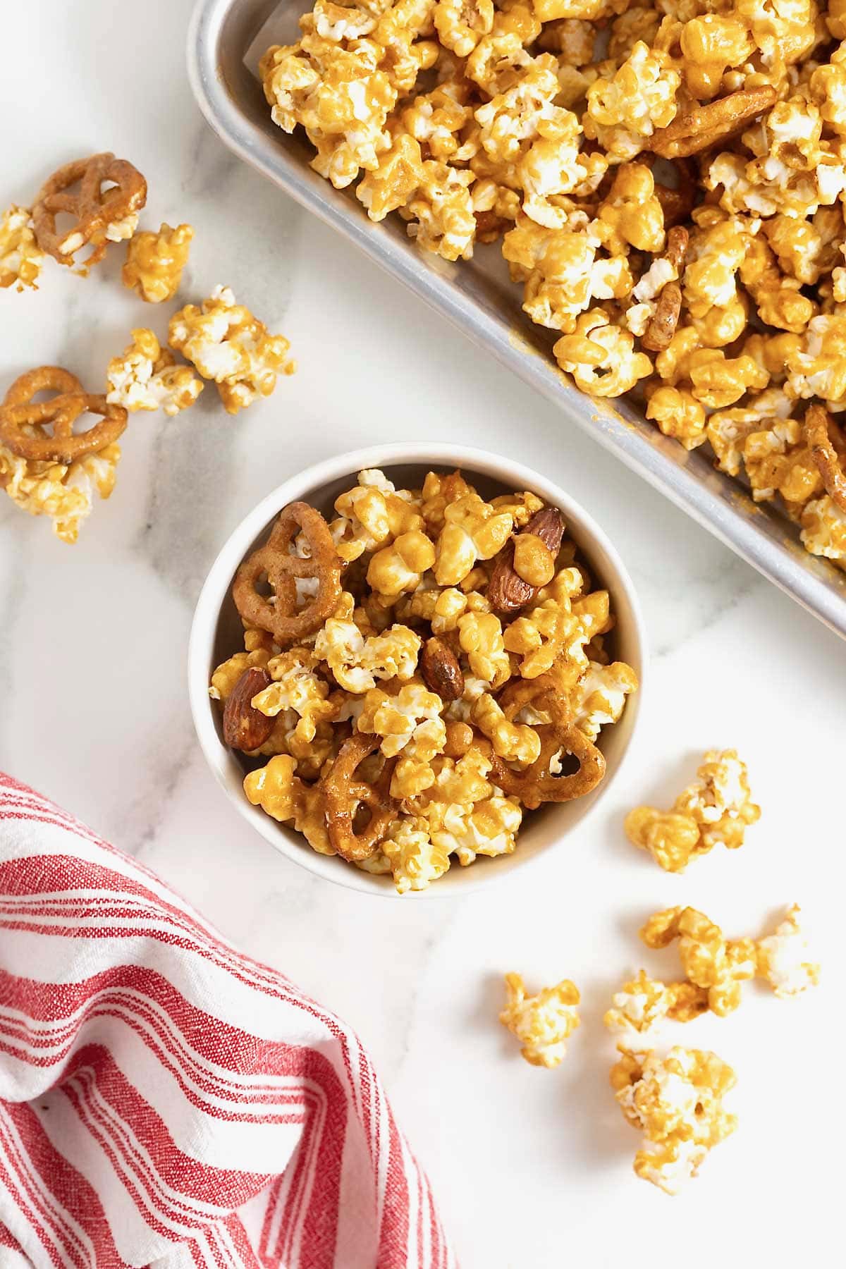 A white bowl of caramel corn mix on a white marble counter.