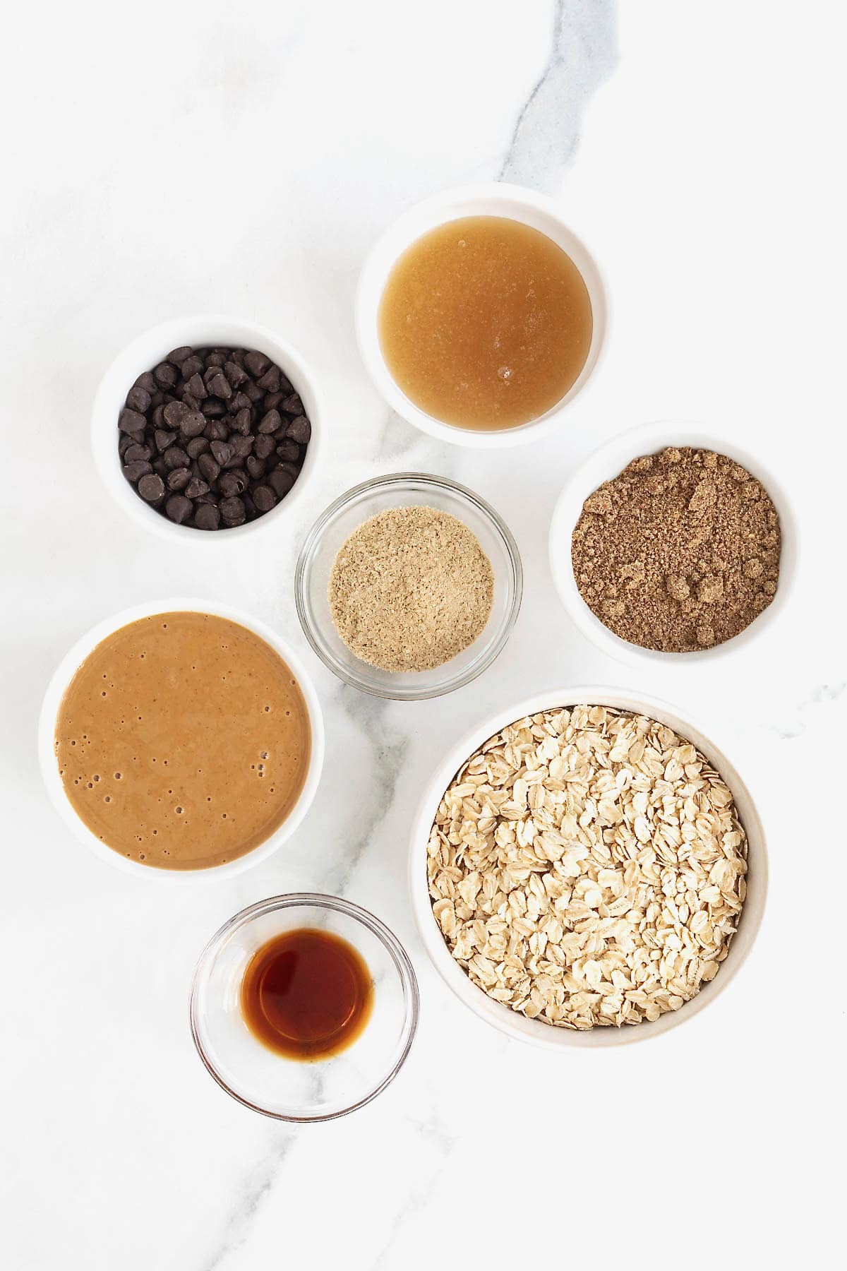 Ingredients to make lactation bites in small glass dishes on a white marble counter.