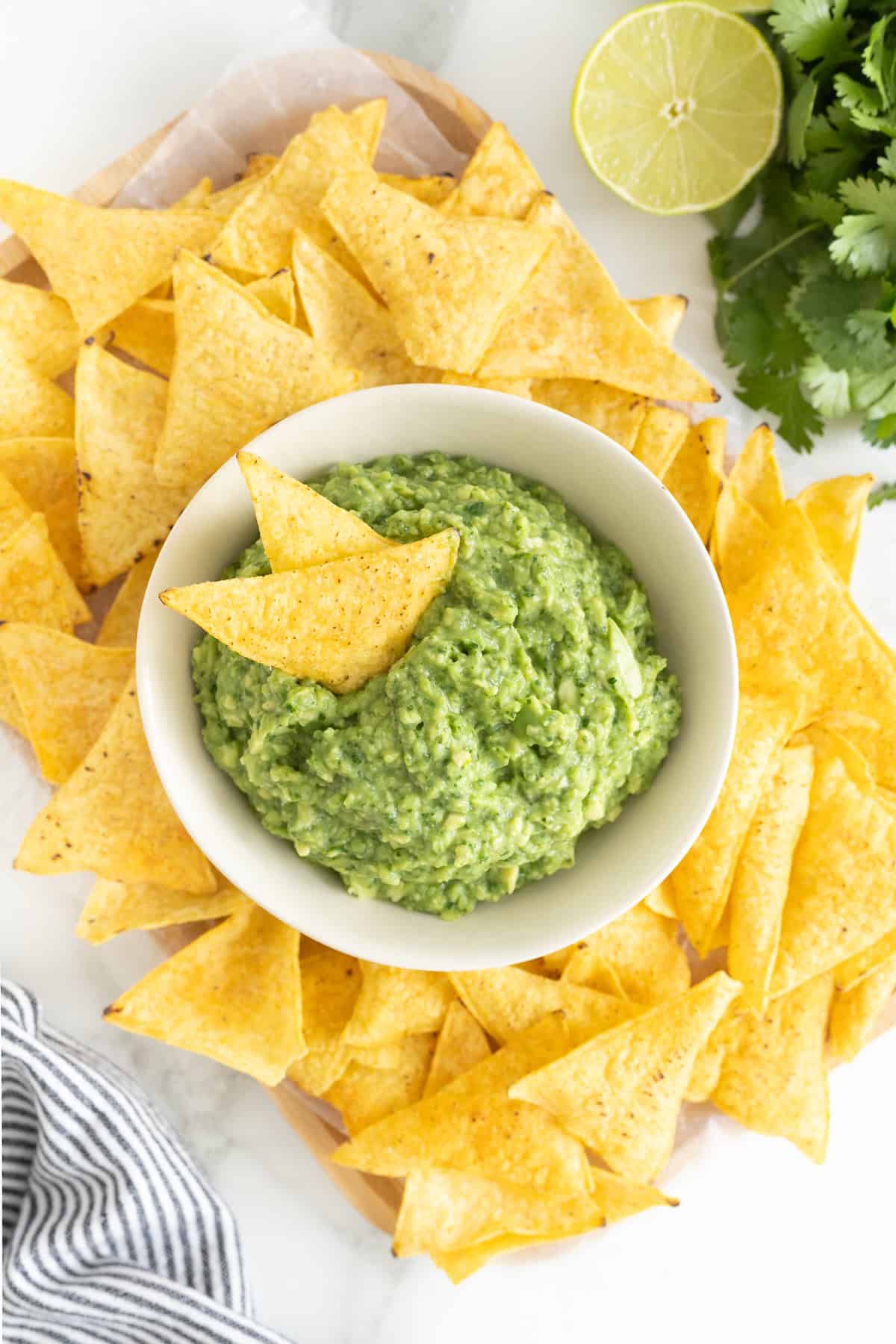A white bowl of guacamole surrounded by tortilla chips.
