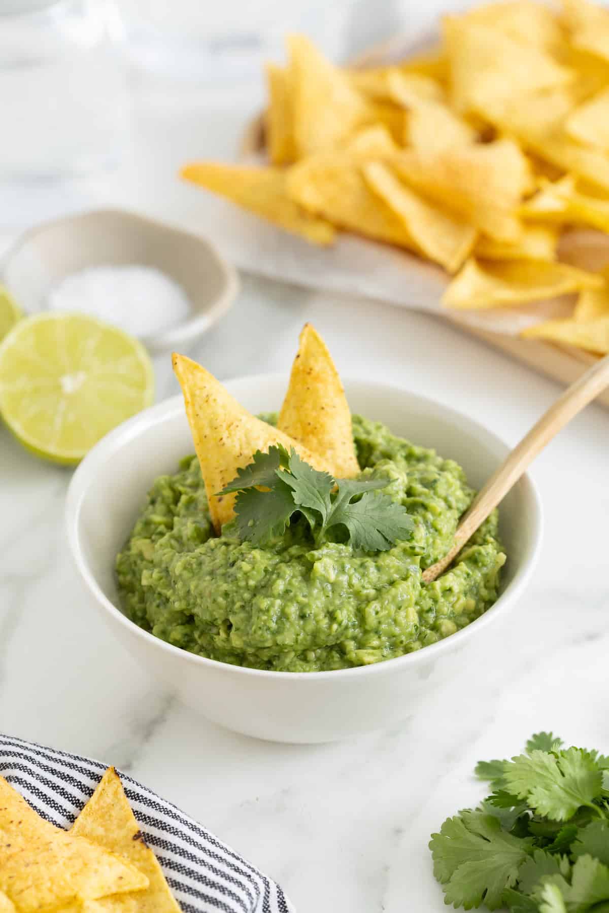 Two corn tortilla chips sticking out of a white bowl of guacamole.