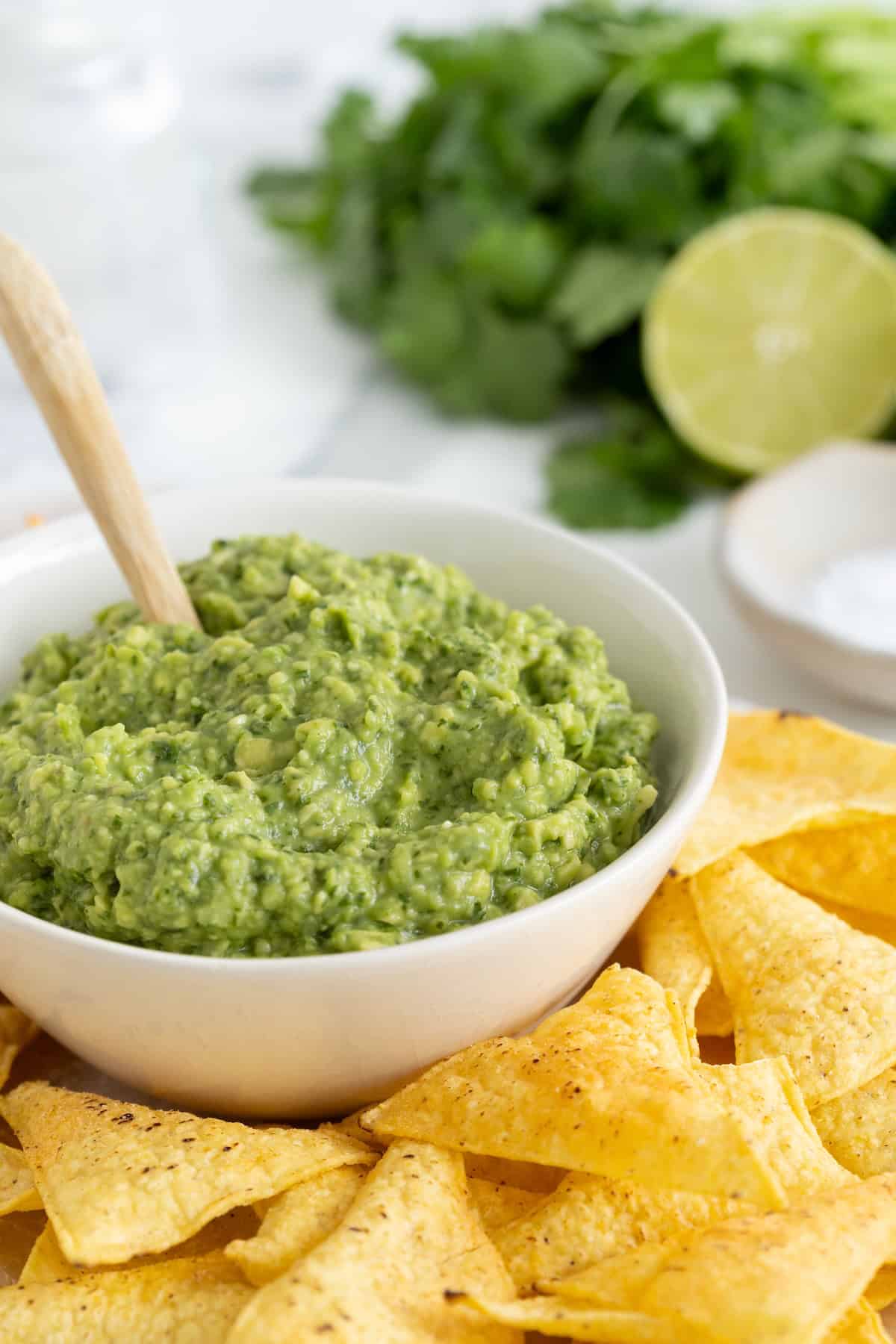 A white bowl of guacamole surrounded by tortilla chips. A small wooden spoon is sticking out of the guacamole.