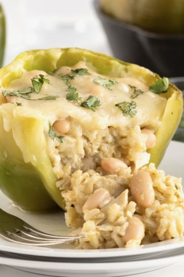 A stuffed green pepper with rice, white beans and white cheese melted on top. The pepper is on a small white plate with fork next to it on the left.
