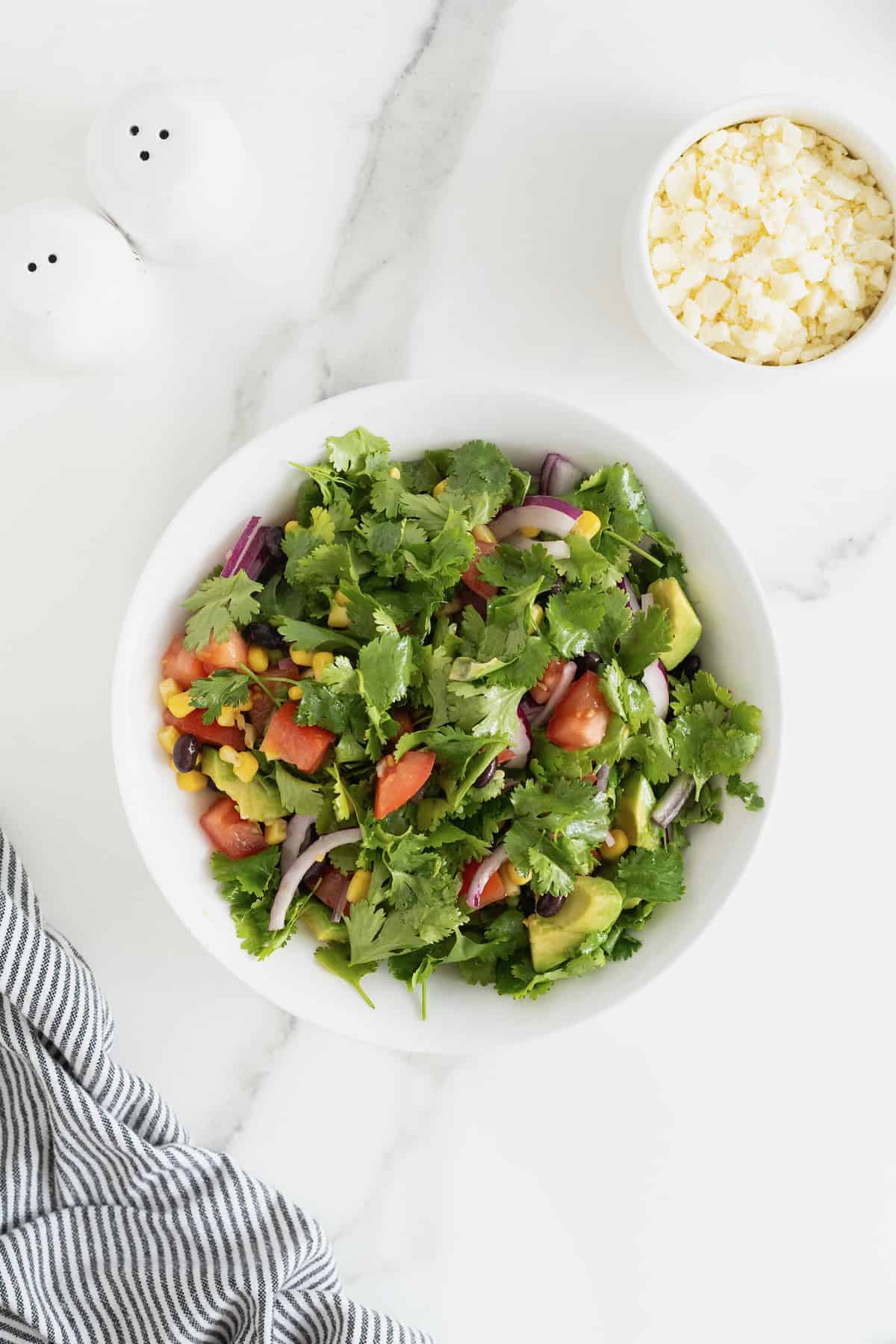 A large white serving bowl of cilantro avocado salad with chopped tomatoes and sliced red onion.