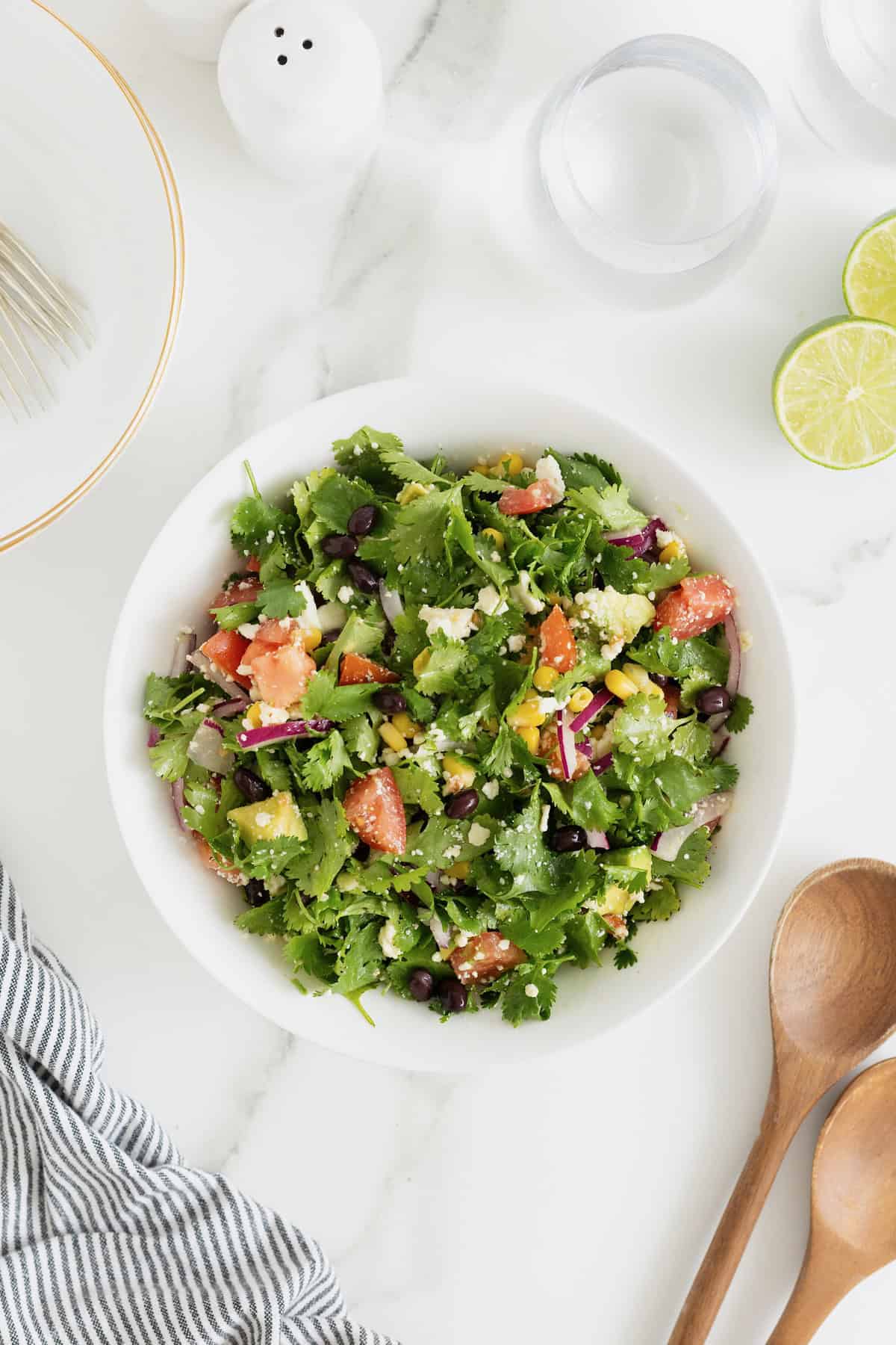 A large white serving bowl of cilantro avocado salad with chopped tomatoes and sliced red onion.