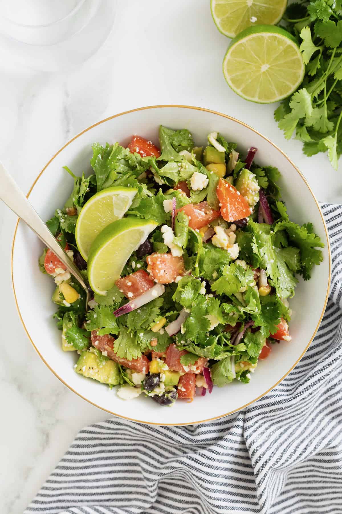 A large white serving bowl of cilantro avocado salad with chopped tomatoes and sliced red onion. There is a metal fork sticking out of the bowl.