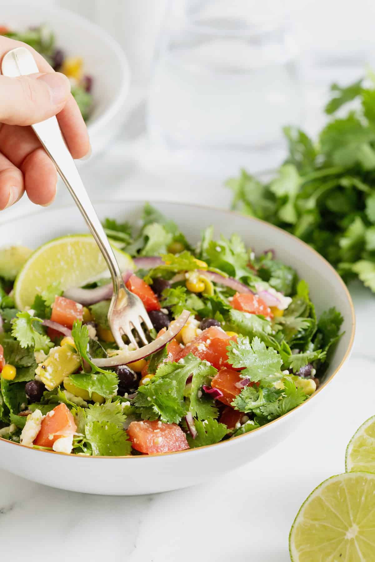 A hand holding a fork in a white bowl of cilantro avocado salad.