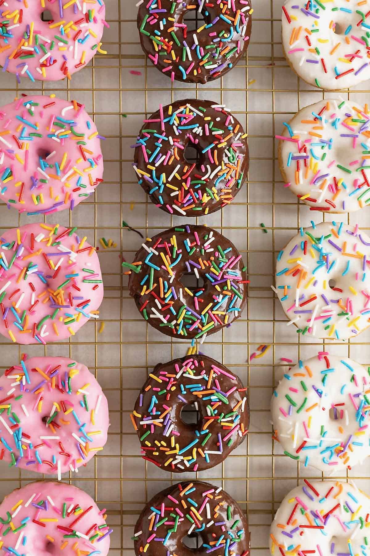 Strawberry, chocolate and vanilla iced donuts on a wire cooling rack.