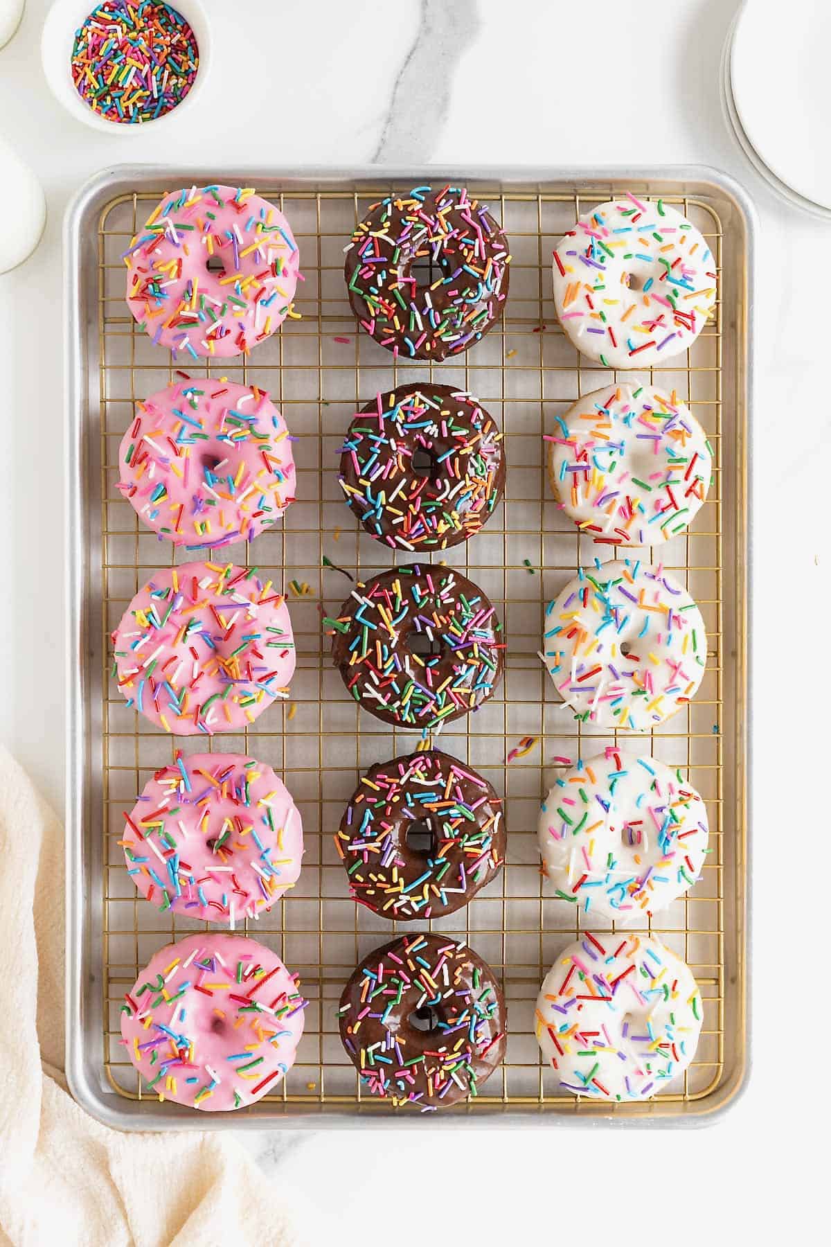 Strawberry, chocolate and vanilla iced donuts on a wire cooling rack in a rimmed baking sheet.