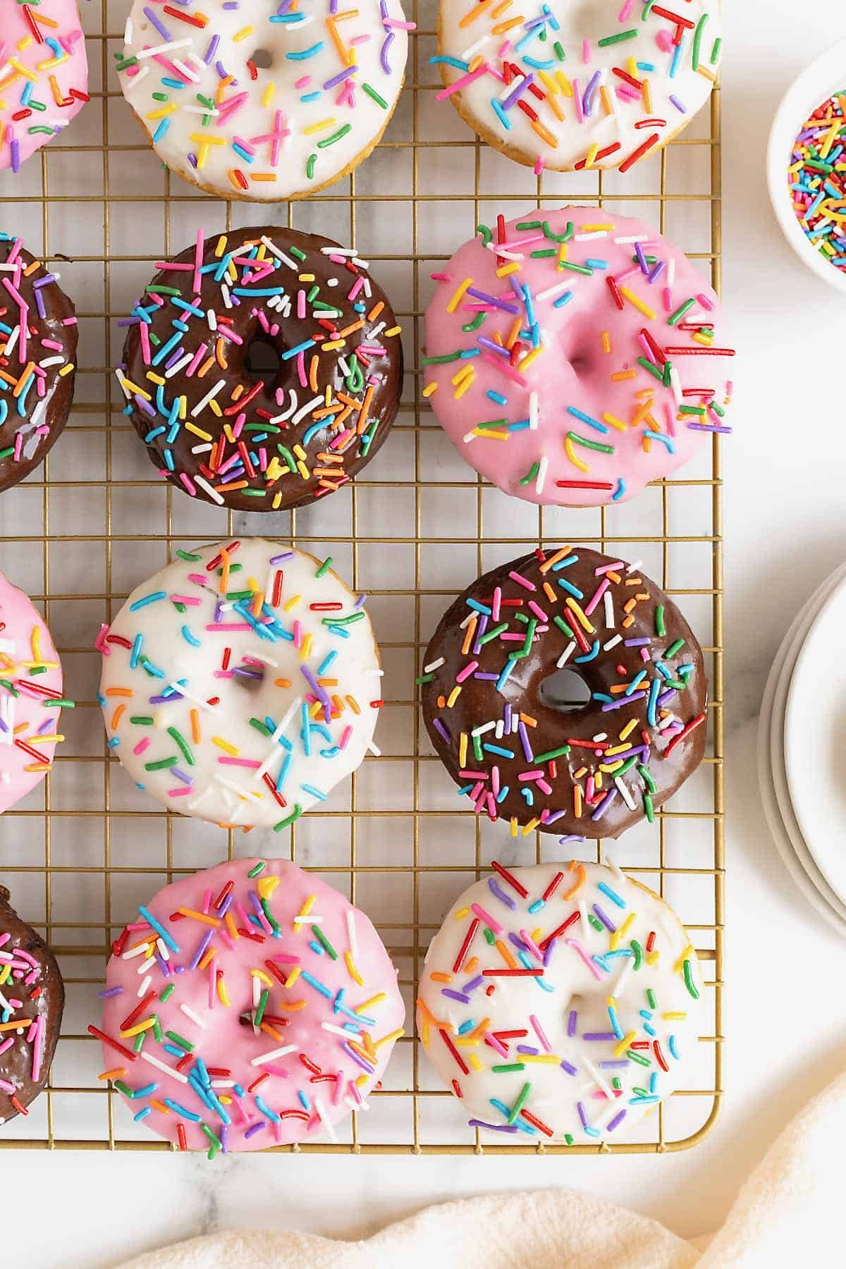Strawberry, chocolate and vanilla iced donuts on a wire cooling rack.