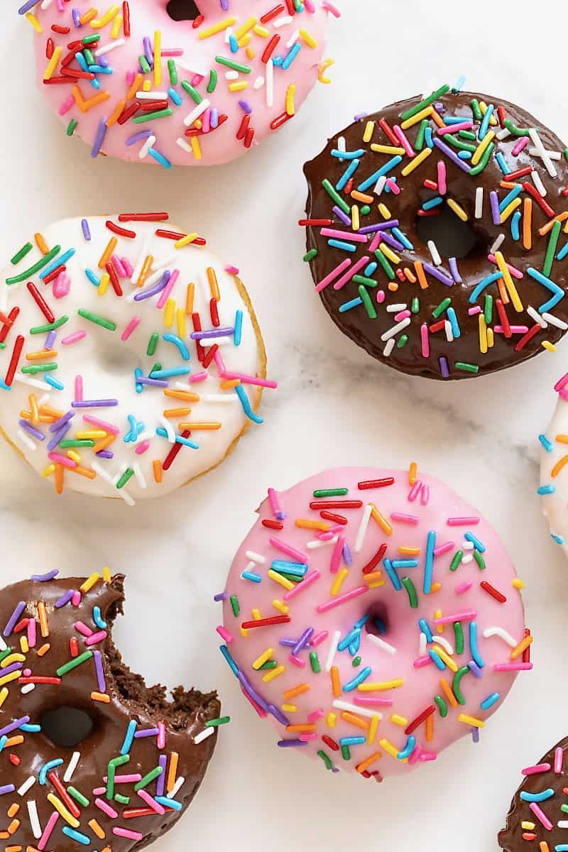 Strawberry, chocolate and vanilla iced donuts on a white marble counter.
