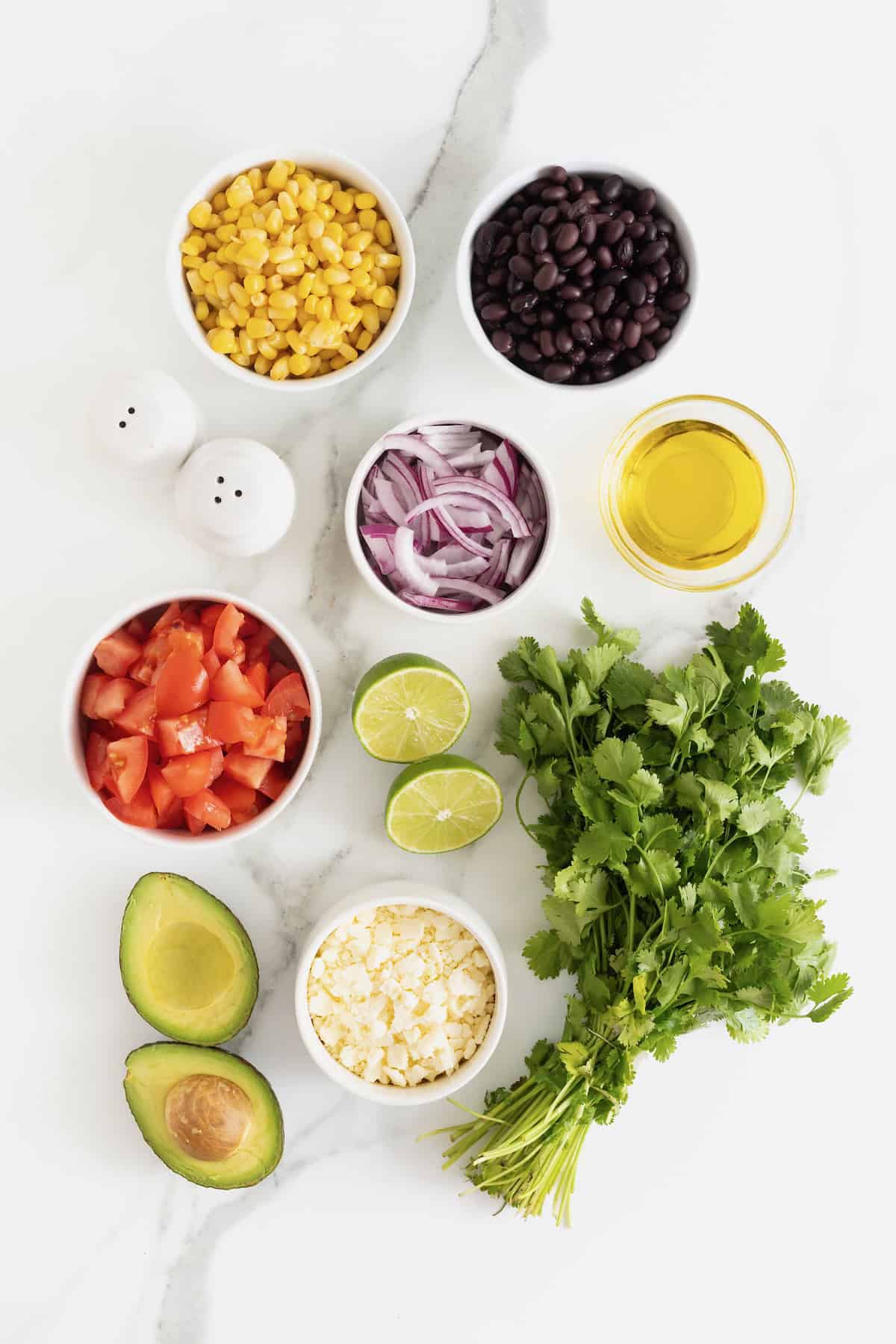 Ingredients to make cilantro avocado salad in small glass dishes on a white marble counter.