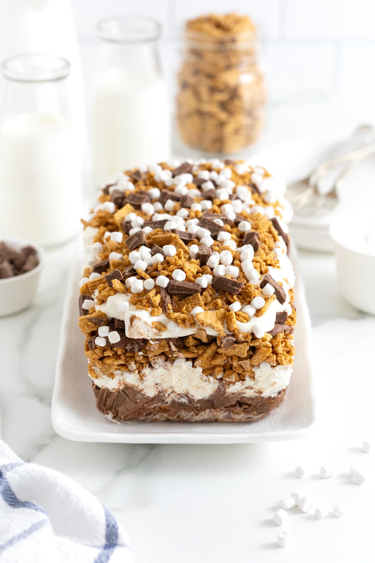 A layered s'mores ice cream cake topped with marshmallow bits, chocolate chunks and 