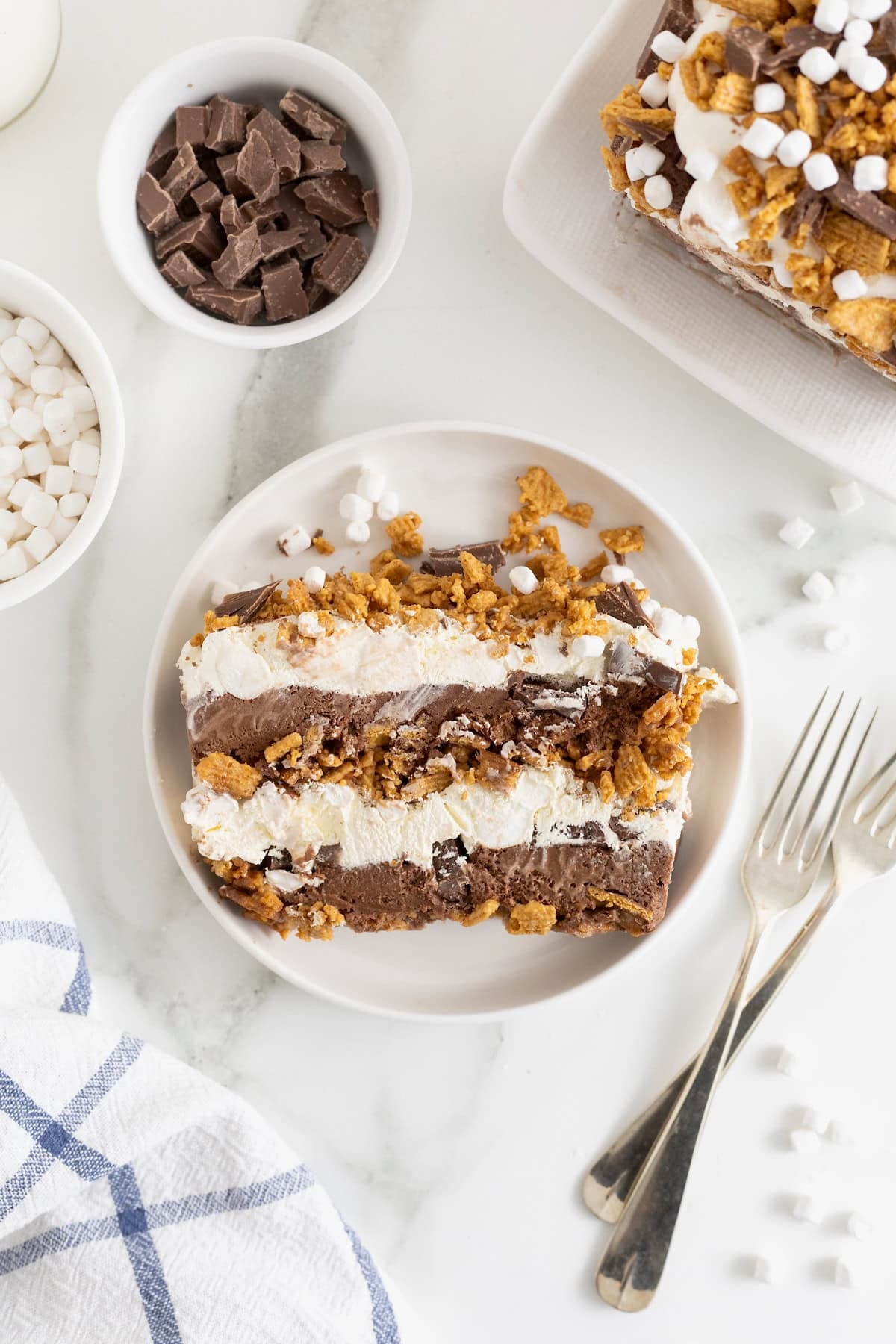 A slice of S'mores Pie on a white plate. There are two forks next to the plate.