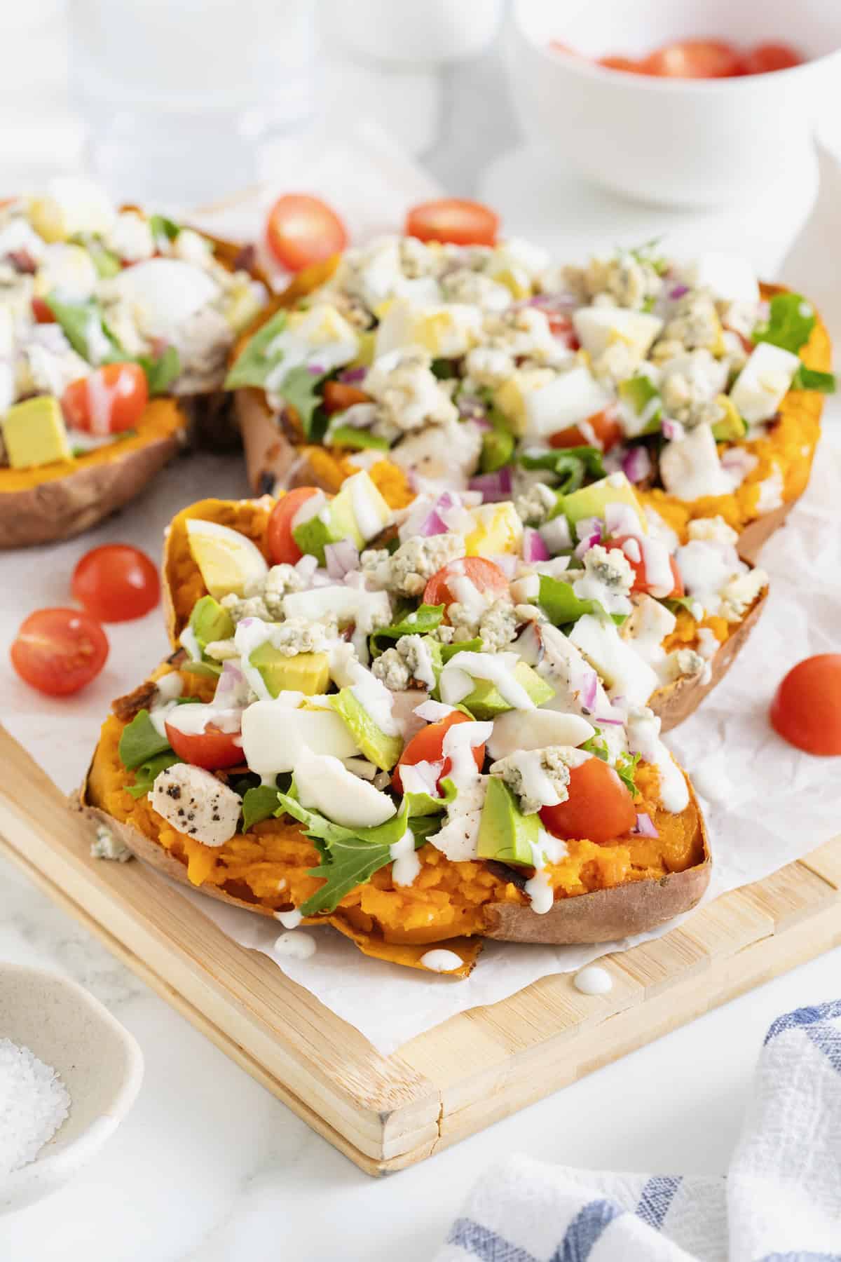 Three Cobb Salad Sweet Potatoes on a parchment lined wooden cutting board.
