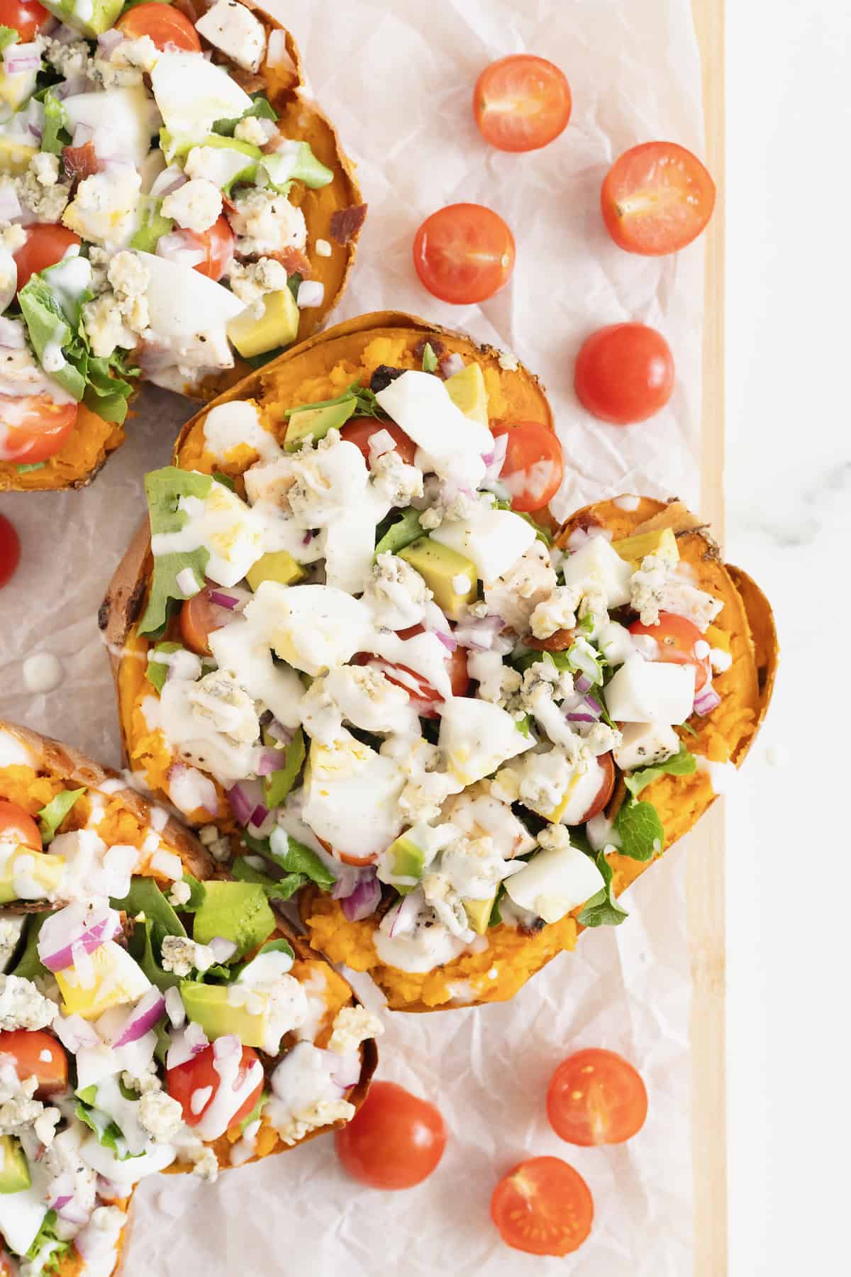 Three Cobb Salad Sweet Potatoes on a parchment lined wooden cutting board.