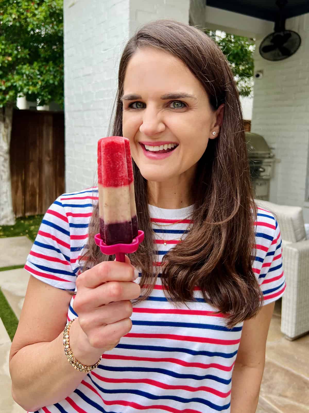 Maegan Brown wearing a red, white and blue striped short sleeve shirt holding a tri-color patriotic fruit pop.