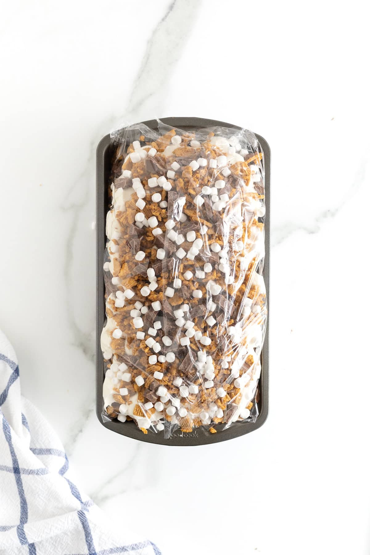 Plastic wrap over a loaf pan of S'mores Ice Cream Cake.